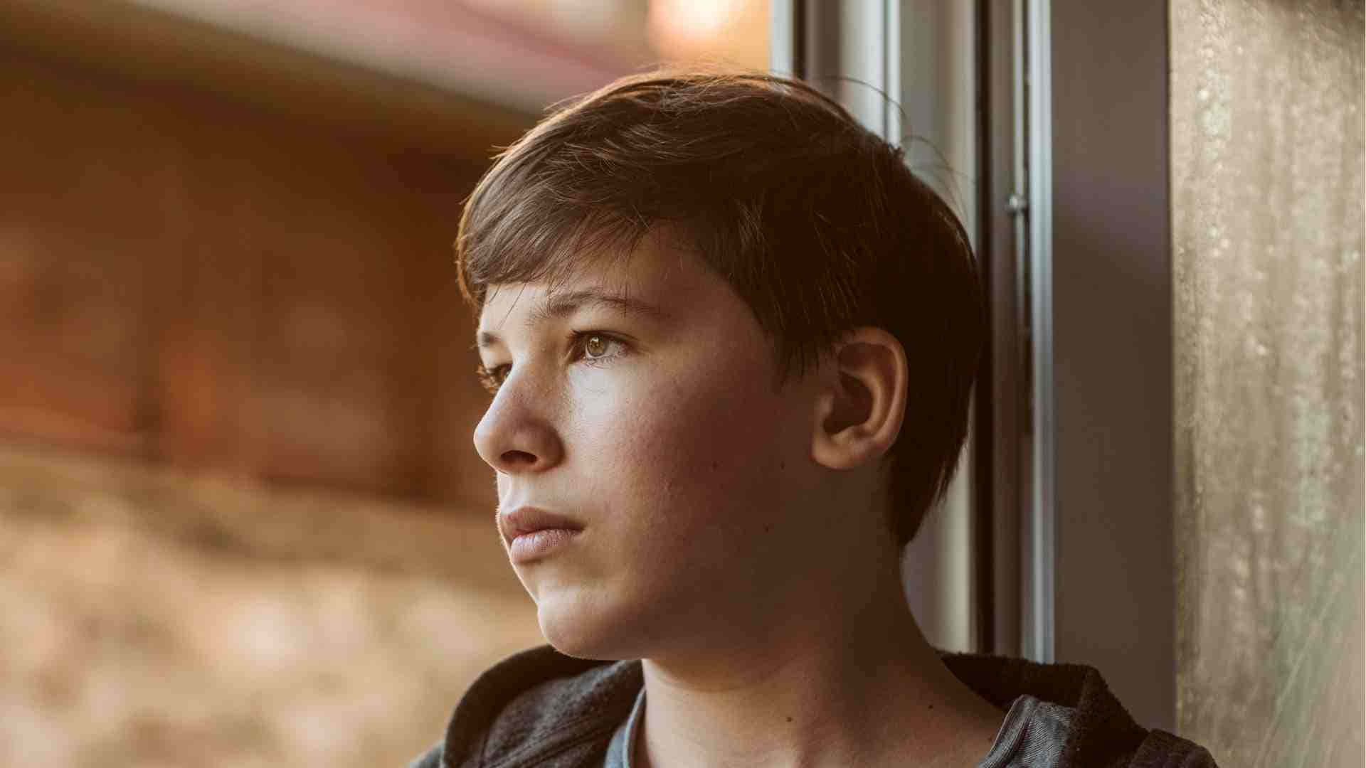 神情孤寂的熱血少年 壁紙 — 一個小男孩沉思地望著窗外，溫暖的金色陽光灑在他身上，突顯了他沉思的表情。