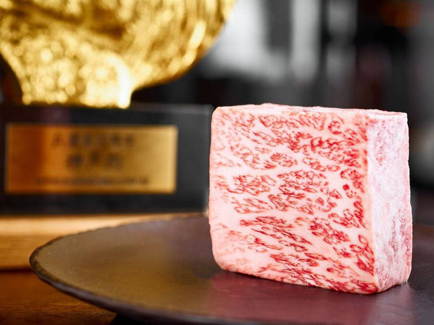 金色獎盃旁邊的一塊高級大理石紋牛肉立方體。