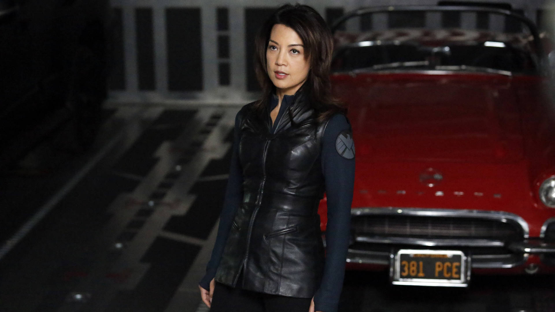 身穿黑色皮背心的女性站在車庫中紅色經典汽車旁。 — 波姬·小絲 GIF 壁紙