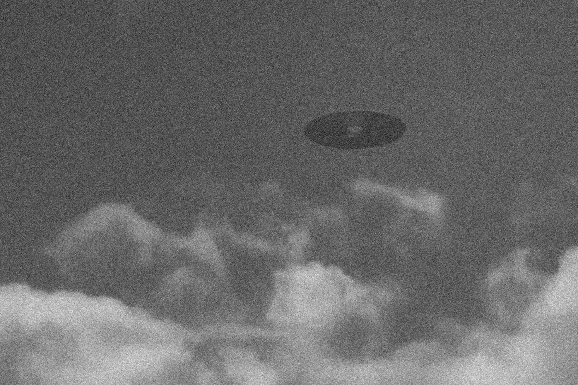 在粗糙的黑白圖像中，飛碟盤旋在烏雲之上。