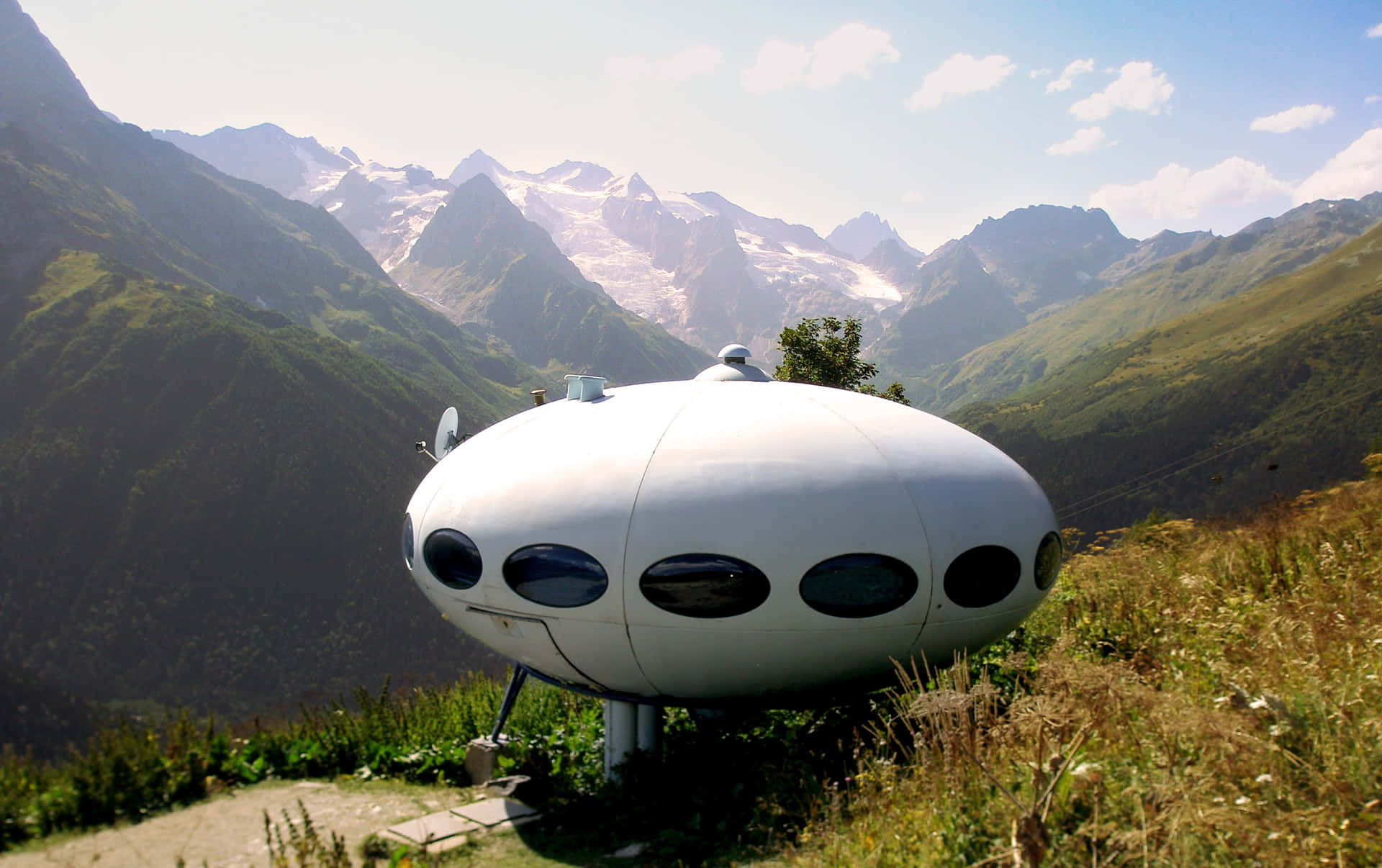 白色UFO形狀小屋位於山脊上，背後有白雪覆蓋的山峰。