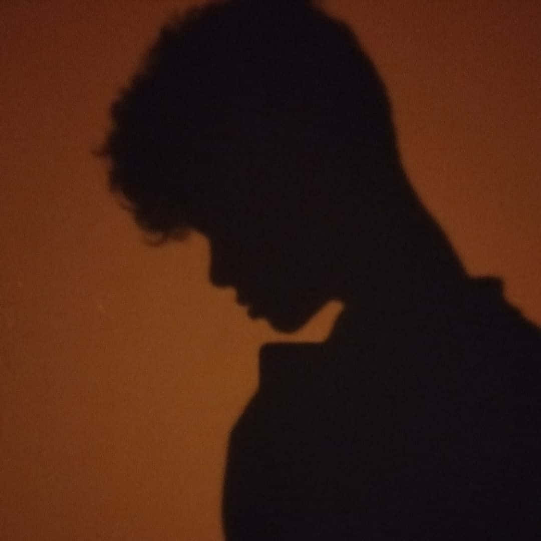 一個有曲髮的人的剪影，襯著橙色牆壁。
