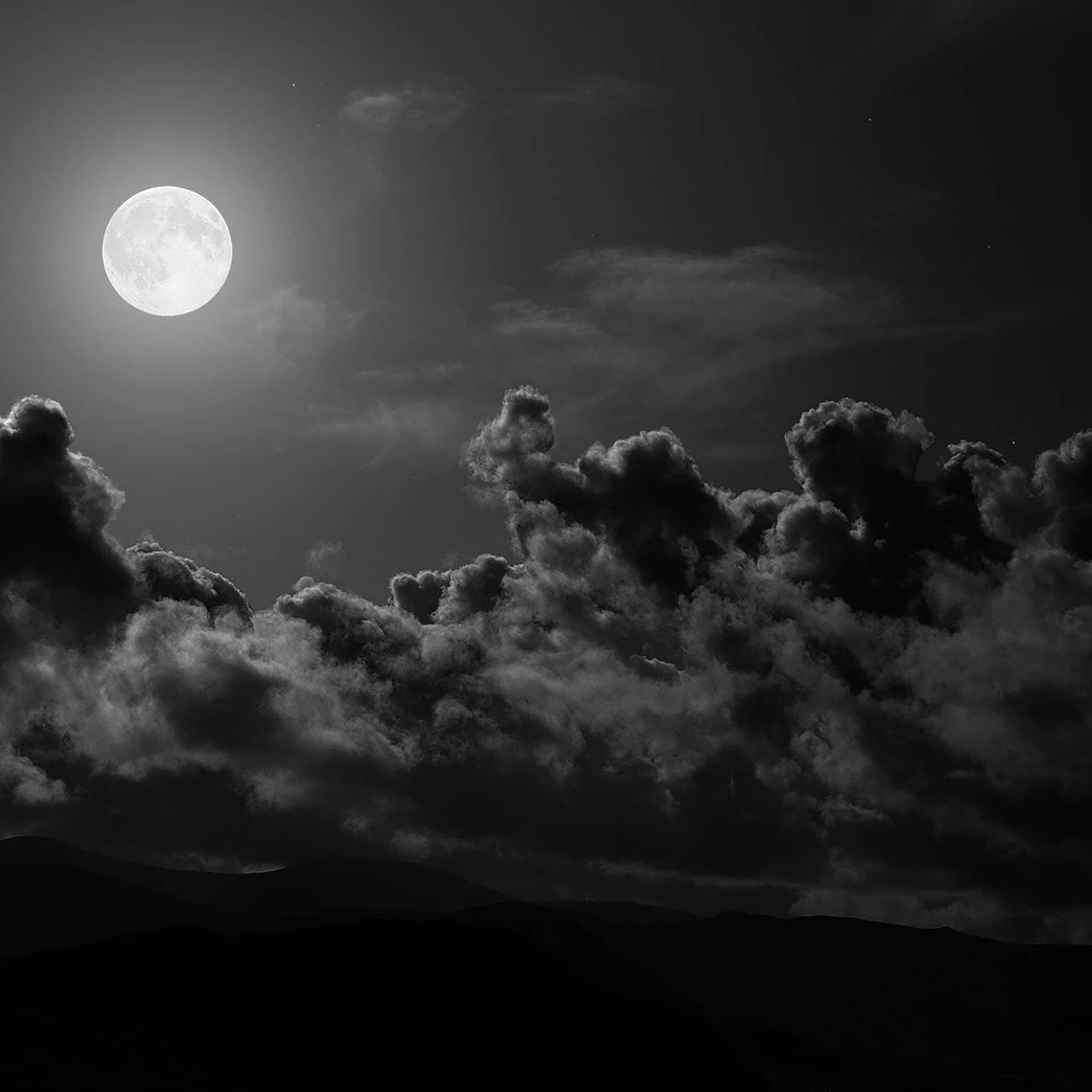 滿月在紋理雲層後發光，照耀夜間山脈