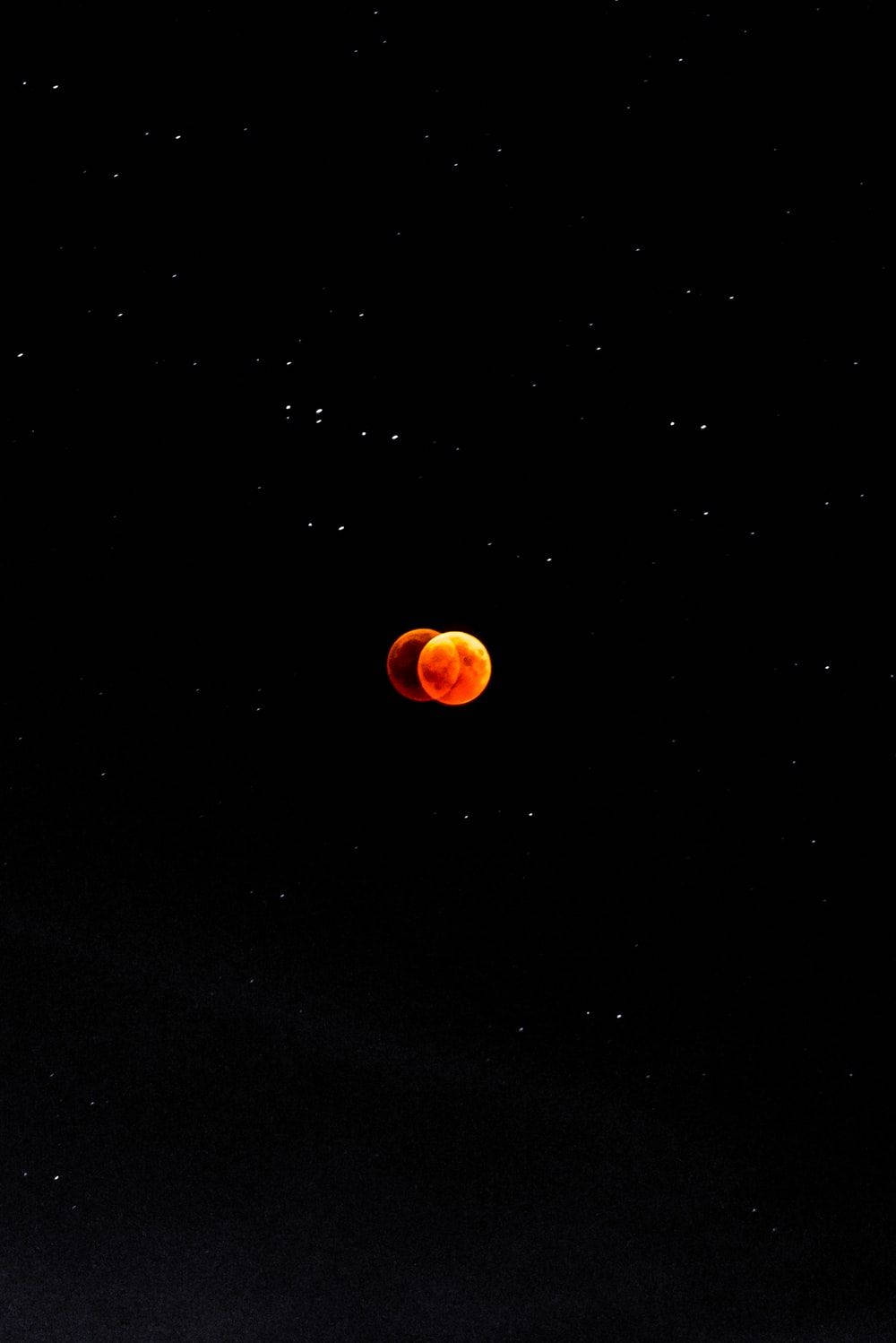 神秘月球連接 - 兩部紅色電話 壁紙 — 血月食在繁星點點的夜空中發出橙色光芒，帶有地球陰影的黑色輪廓。