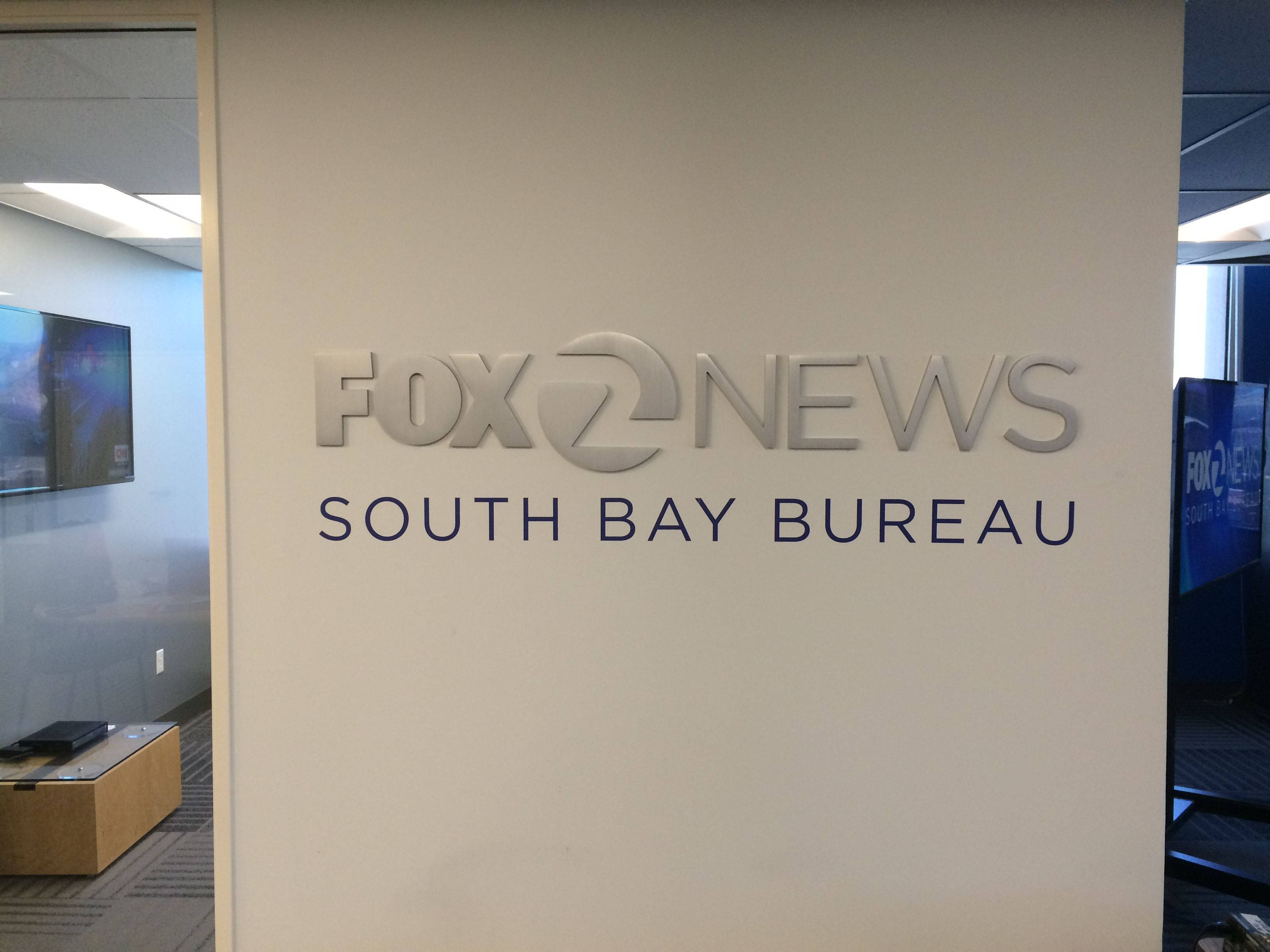 福克斯新聞南灣分局標誌 壁紙 — 一個時尚的銀色Fox News South Bay Bureau標誌安裝在現代辦公空間的米色牆上。