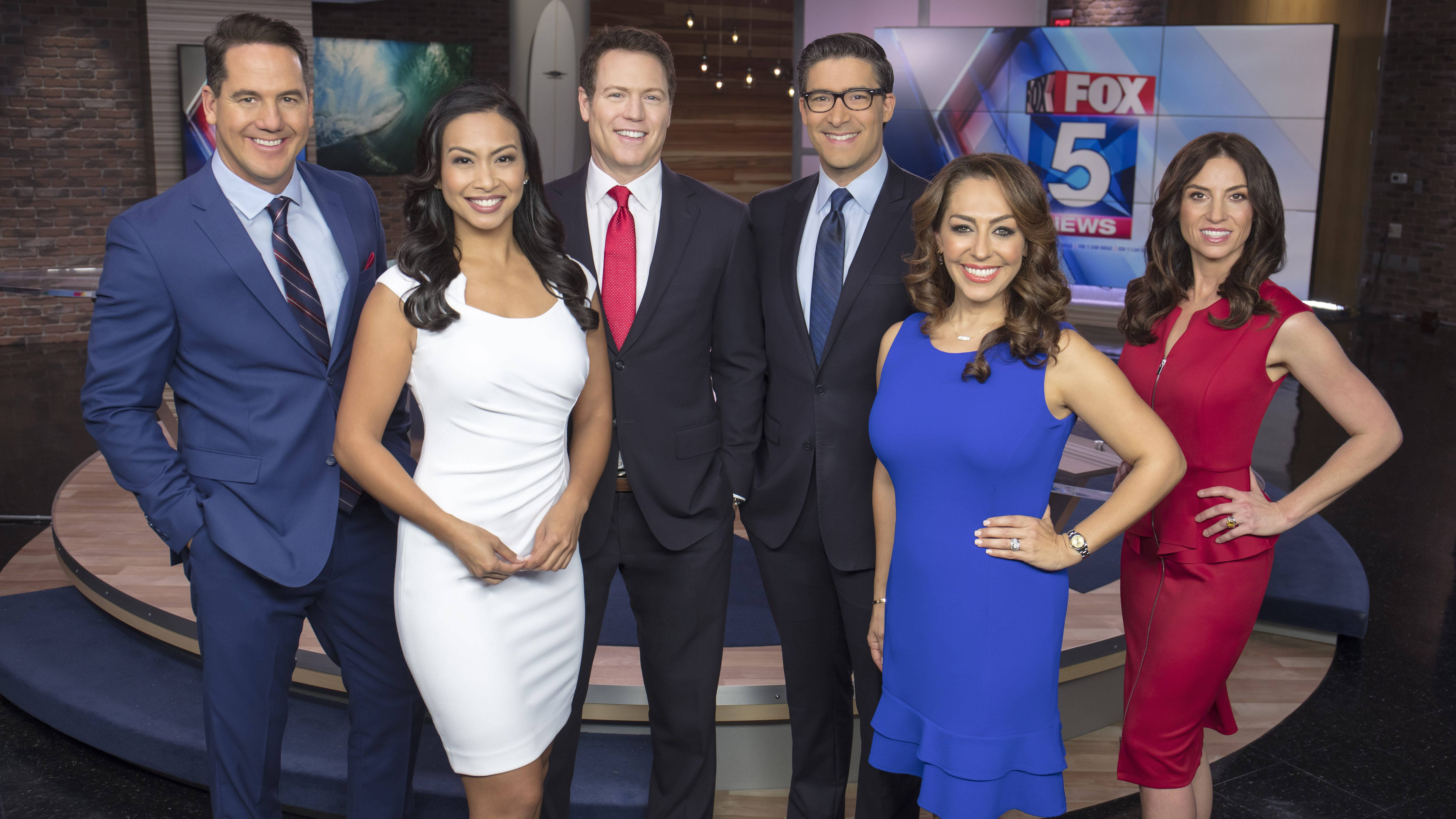福克斯新聞團隊 壁紙 — 六位面帶微笑的新聞主播身著正裝，在設有FOX 5 News背景的現代電視演播室中自信地擺姿勢。