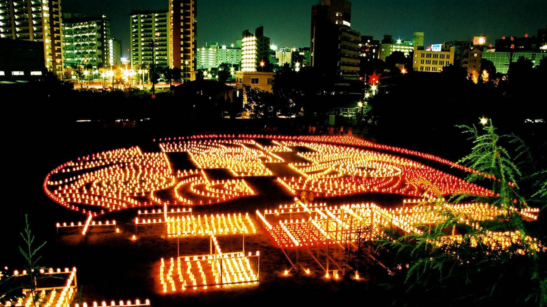 福岡夜景城市燈光 壁紙 — 數千支發光的蠟燭在夜晚的城市天際線下的黑暗田野中形成複雜的圖案。