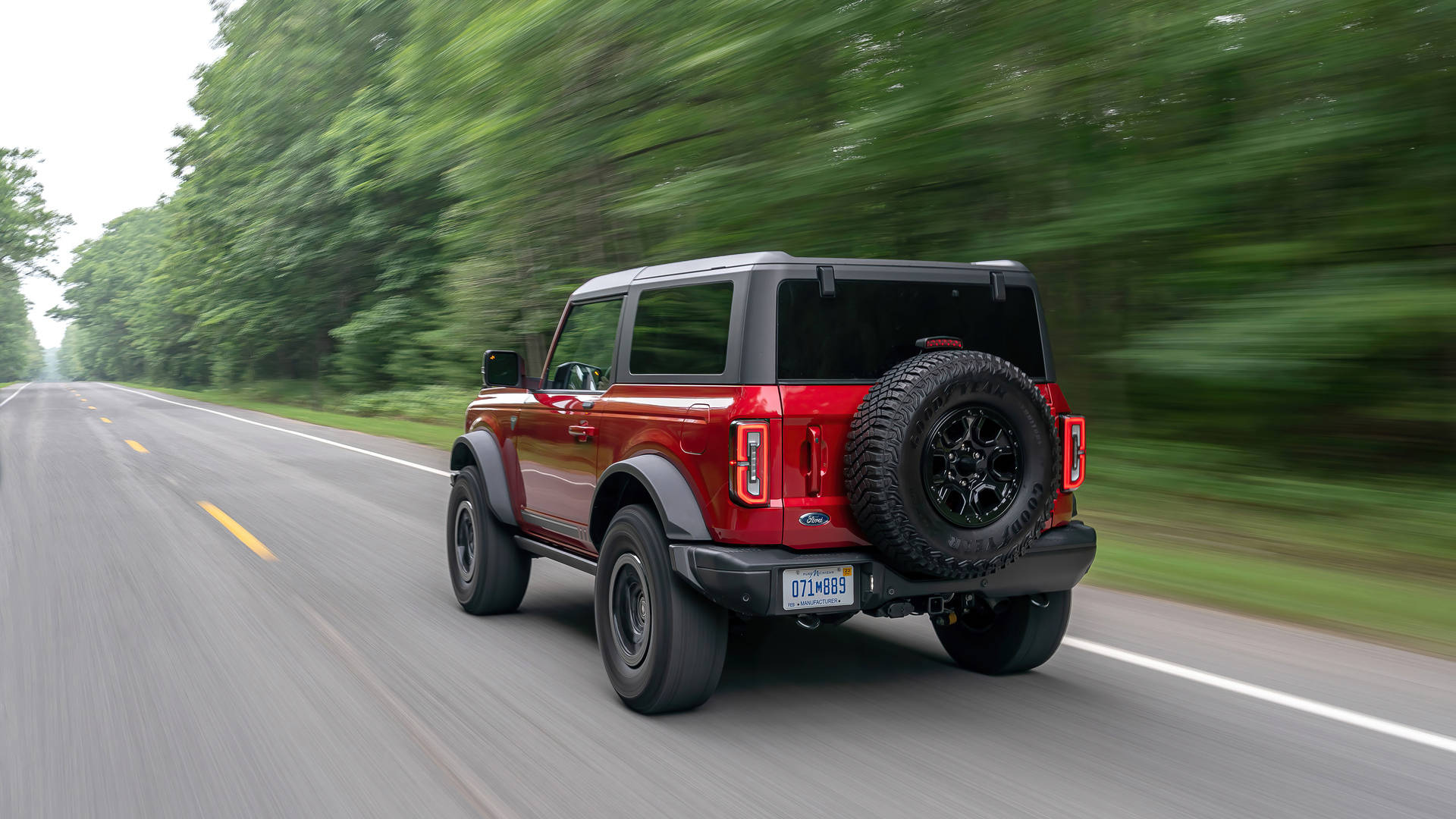 福特 Bronco 紅與磨砂黑 壁紙 — 一輛紅色福特Bronco SUV在樹木成行的道路上疾馳，動態模糊傳達出快速移動的感覺。