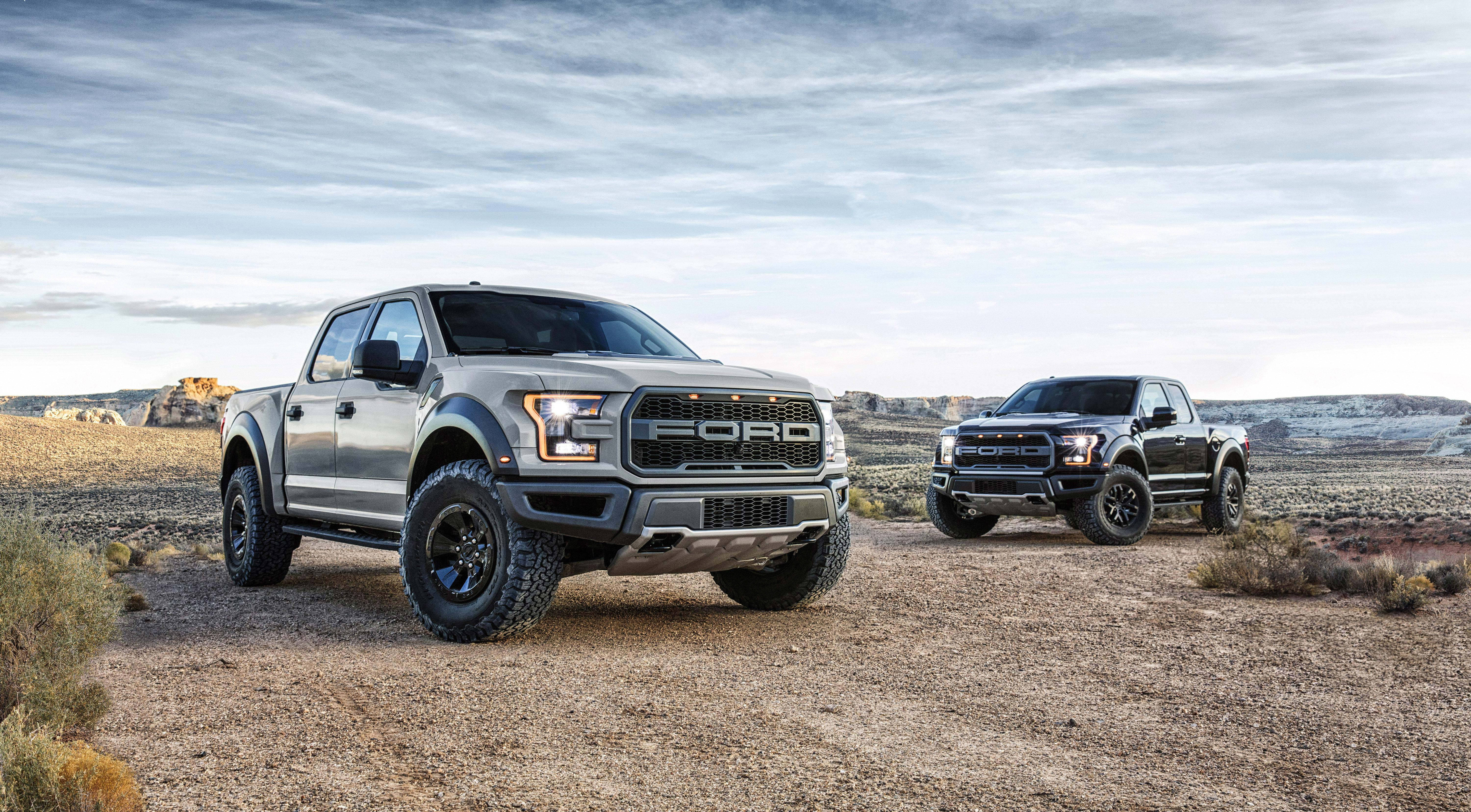 福特Raptor F-150 壁紙 — 兩輛堅固的福特卡車並排停在塵土飛揚的沙漠小徑上，天空多雲。