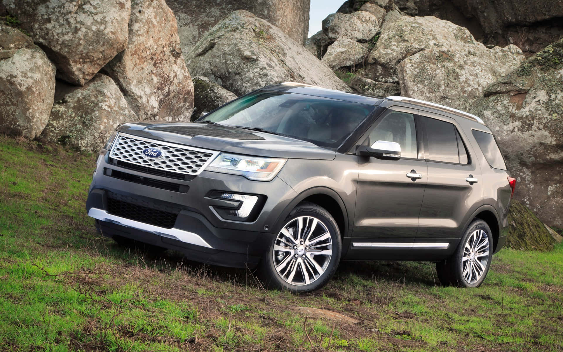 福特探索者SUV行駛於風景路線 壁紙 — 一輛時尚的灰色Ford Explorer SUV停放在草地上，旁邊是巨大的風化岩石，在明亮的日光下。