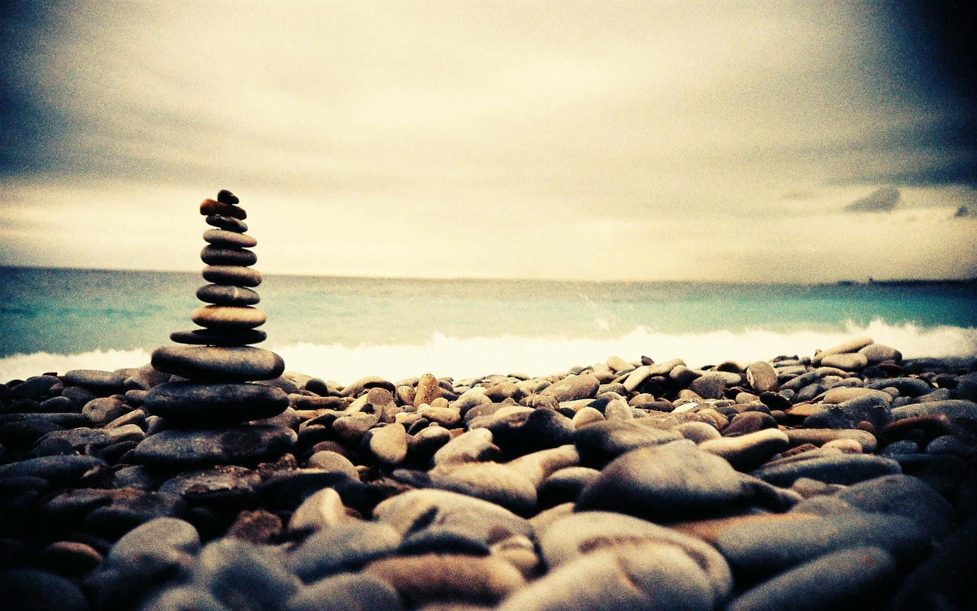 卵石灘上堆疊的石頭，伴隨著海浪和多雲的天空。