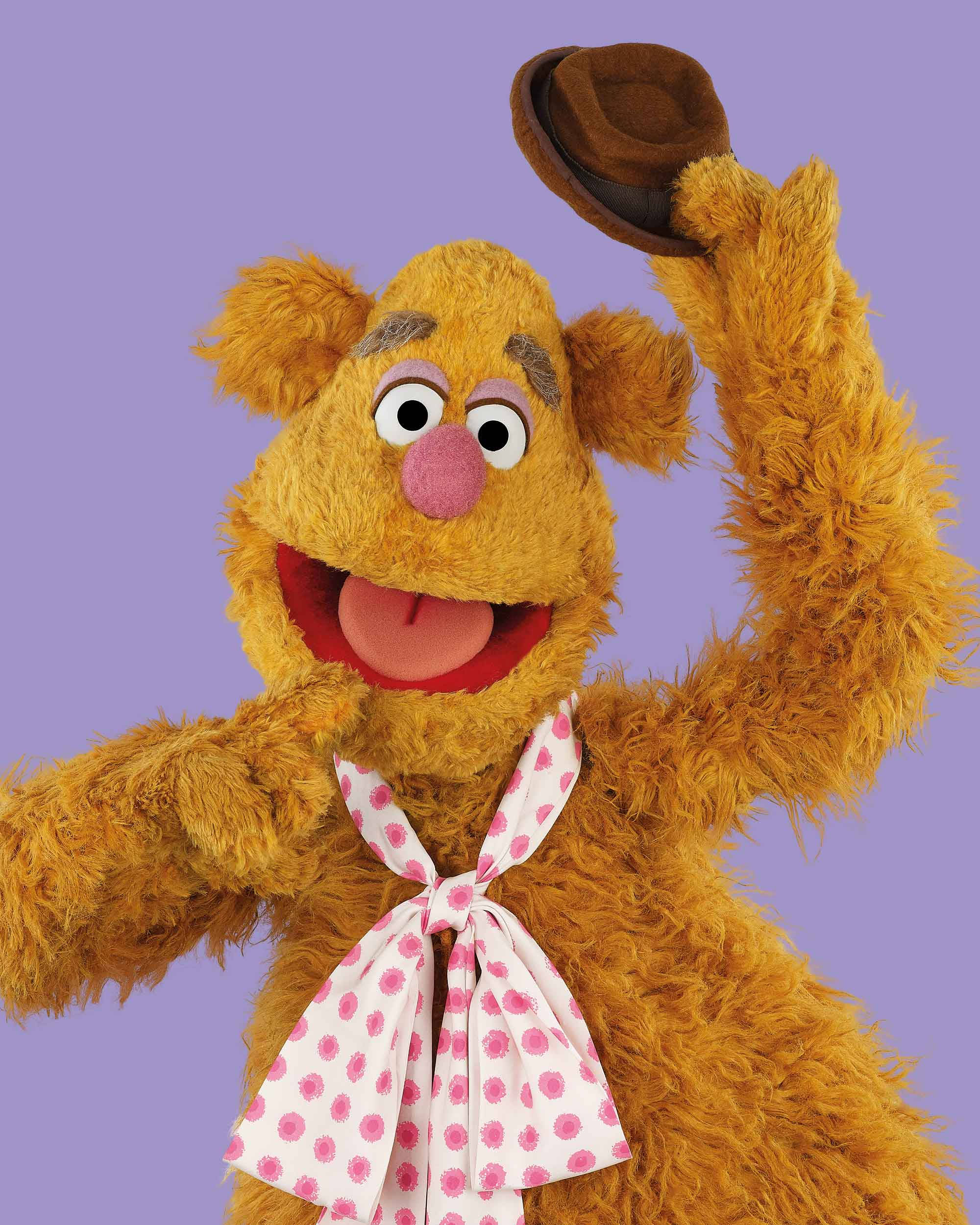 禿頭福滋熊 壁紙 — Fozzie Bear 戴著棕色帽子，在純薰衣草色背景上愉快地揮手。