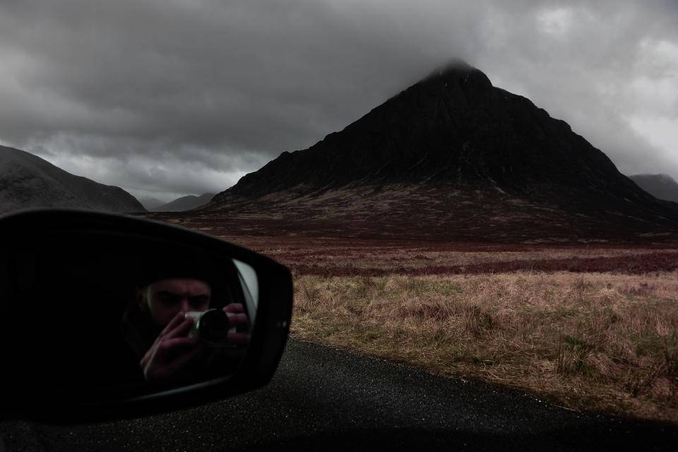 攝影師在陰天透過汽車側鏡拍攝山景。