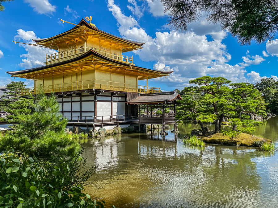 秋日金閣寺的倒影美景 壁紙 — 金色嘅金閣寺喺晴朗藍天同 fluffy 白雲下，倒映喺平靜嘅水面上。