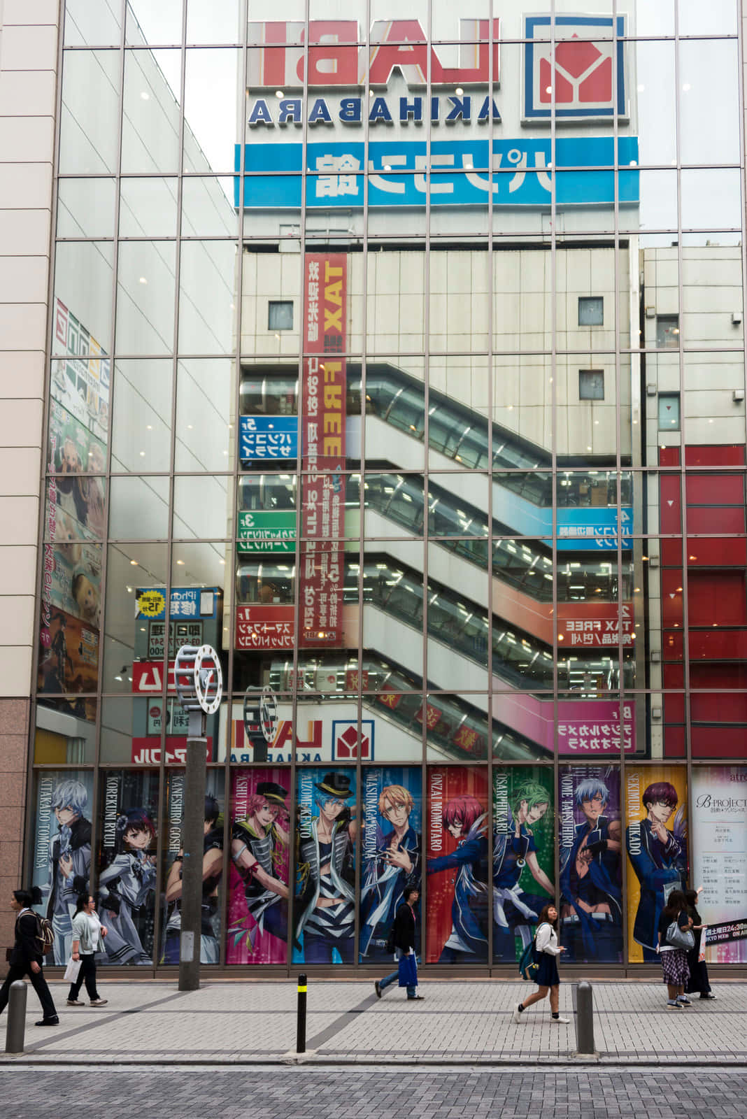 Otaku Culture 桌布 壁紙 — 秋葉原購物中心的玻璃外牆反射著自動扶梯和動漫海報，行人走過。