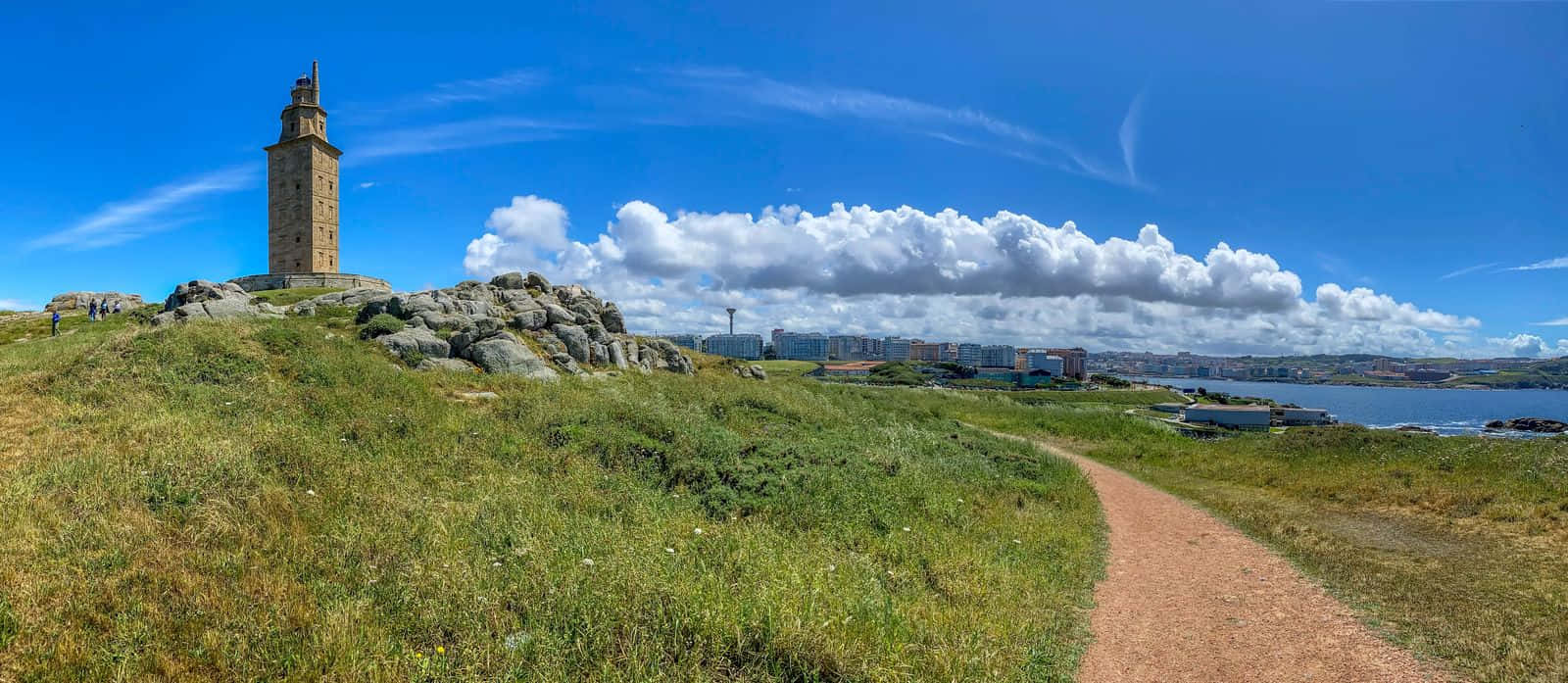 在陽光明媚的天空下，一條風景優美的海岸小徑通往歷史悠久的埃庫萊斯燈塔。