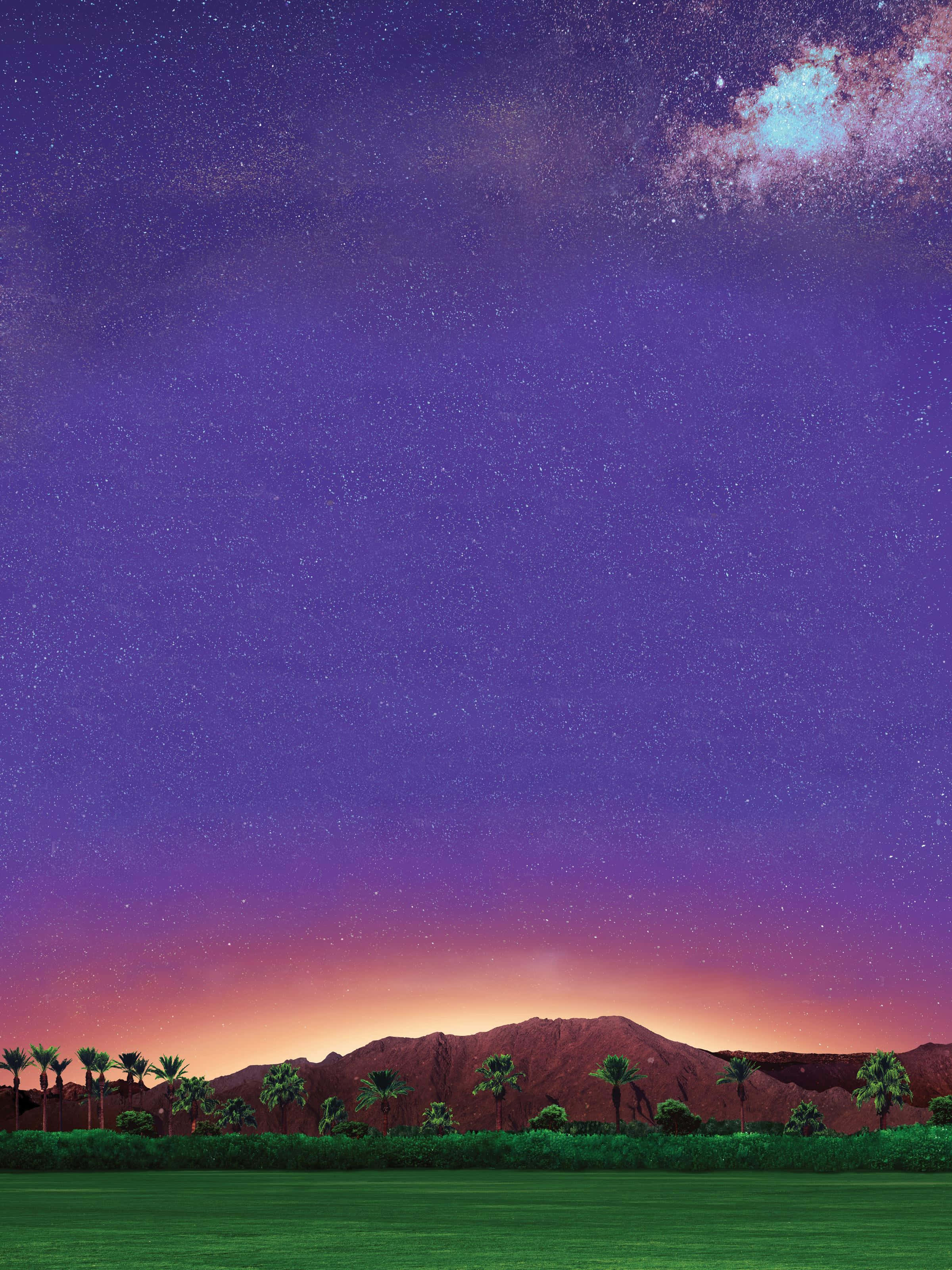 科切拉山谷音樂與藝術節的壯麗場景 壁紙 — 充滿星星的鮮豔夜空和發光的銀河在沙漠景觀上拱起，有棕櫚樹和遠處的山脈。