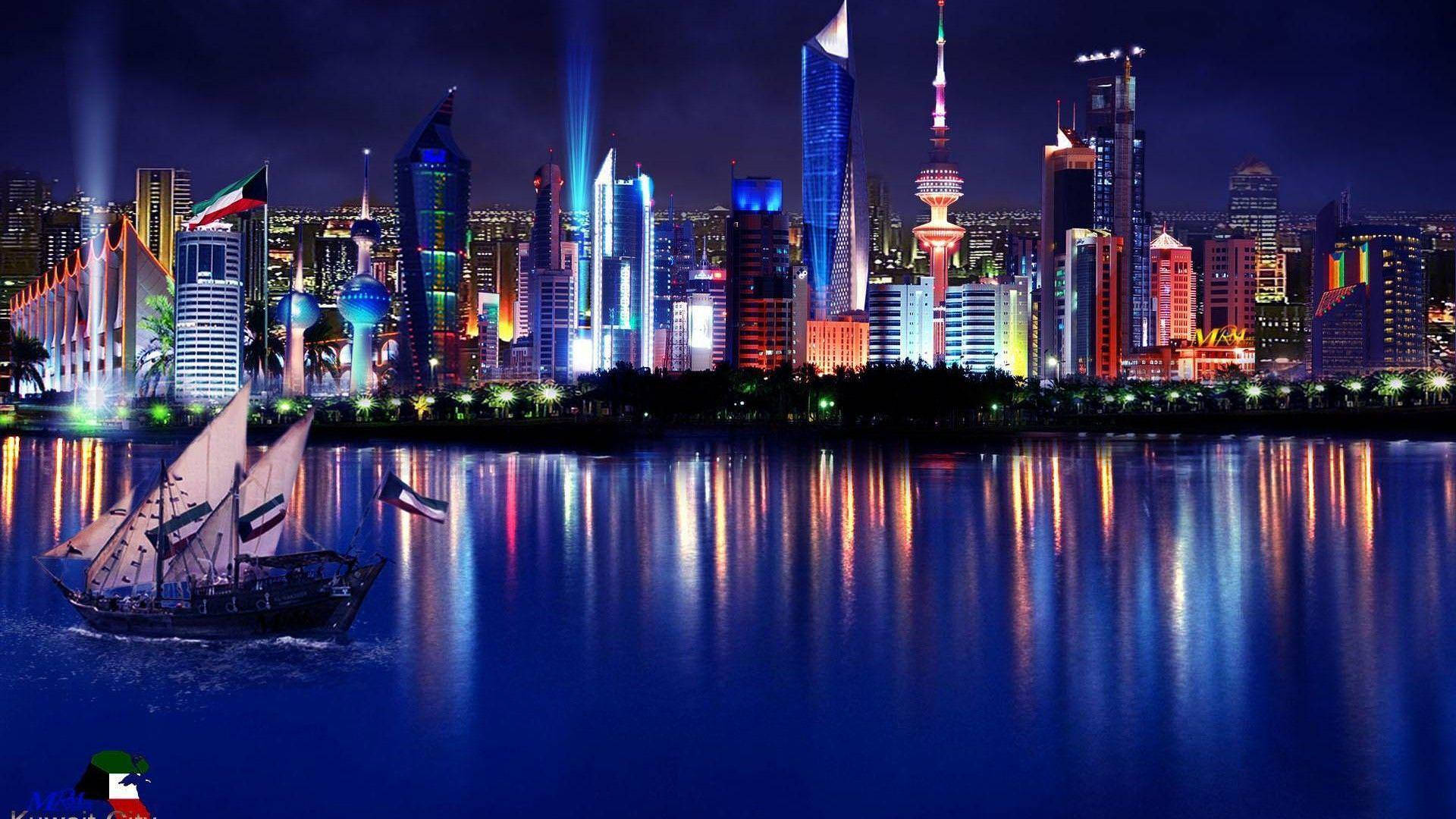 科威特帆船與國旗 壁紙 — 一艘傳統的獨桅帆船在夜晚航行經過燈火輝煌的科威特城市天際線，水面倒映出鮮豔的光影。