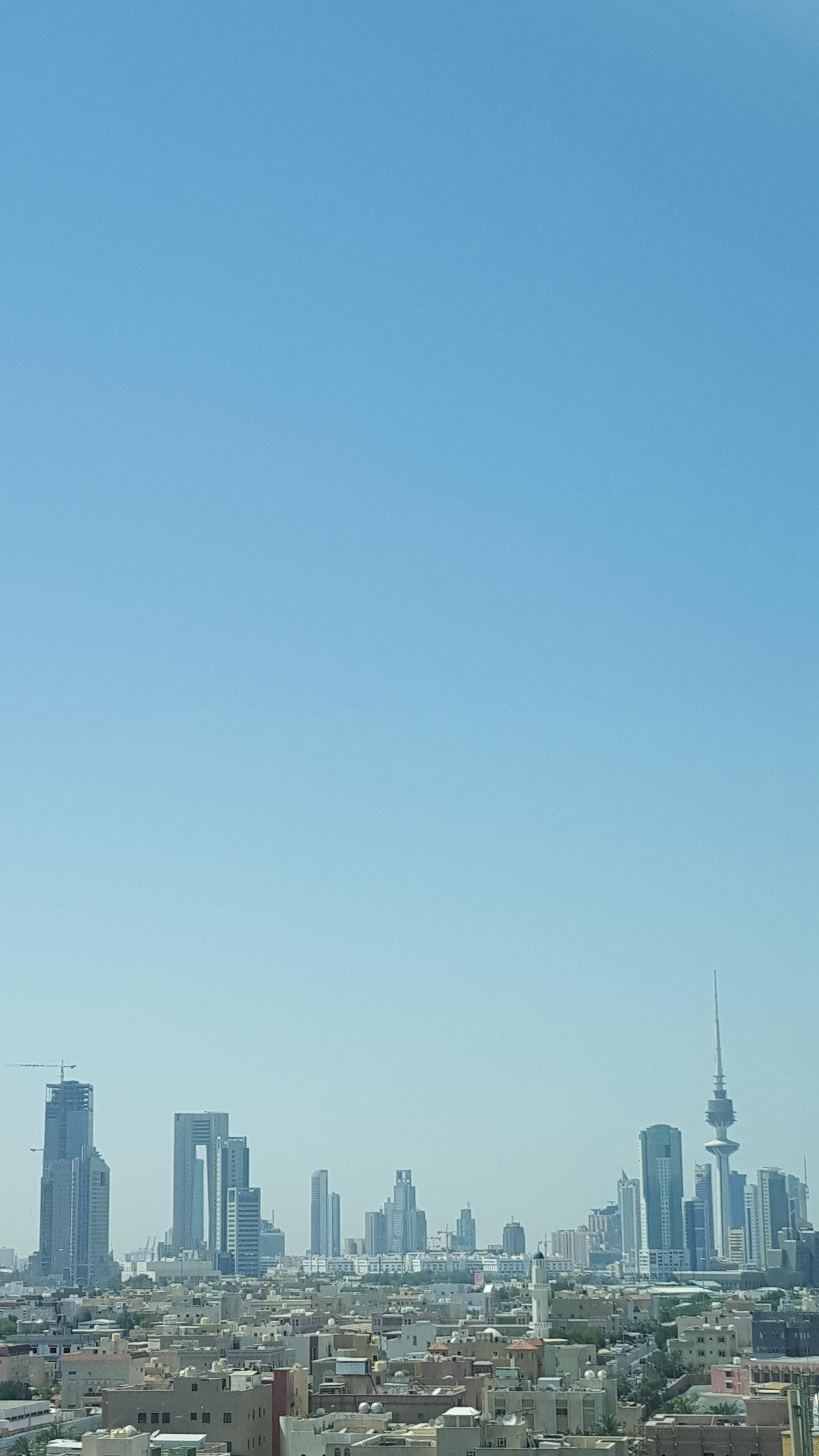 科威特晴空萬里 壁紙 — 現代城市天際線的全景視圖，高聳的摩天大樓和一座突出的塔樓，在廣闊清澈的藍天下。
