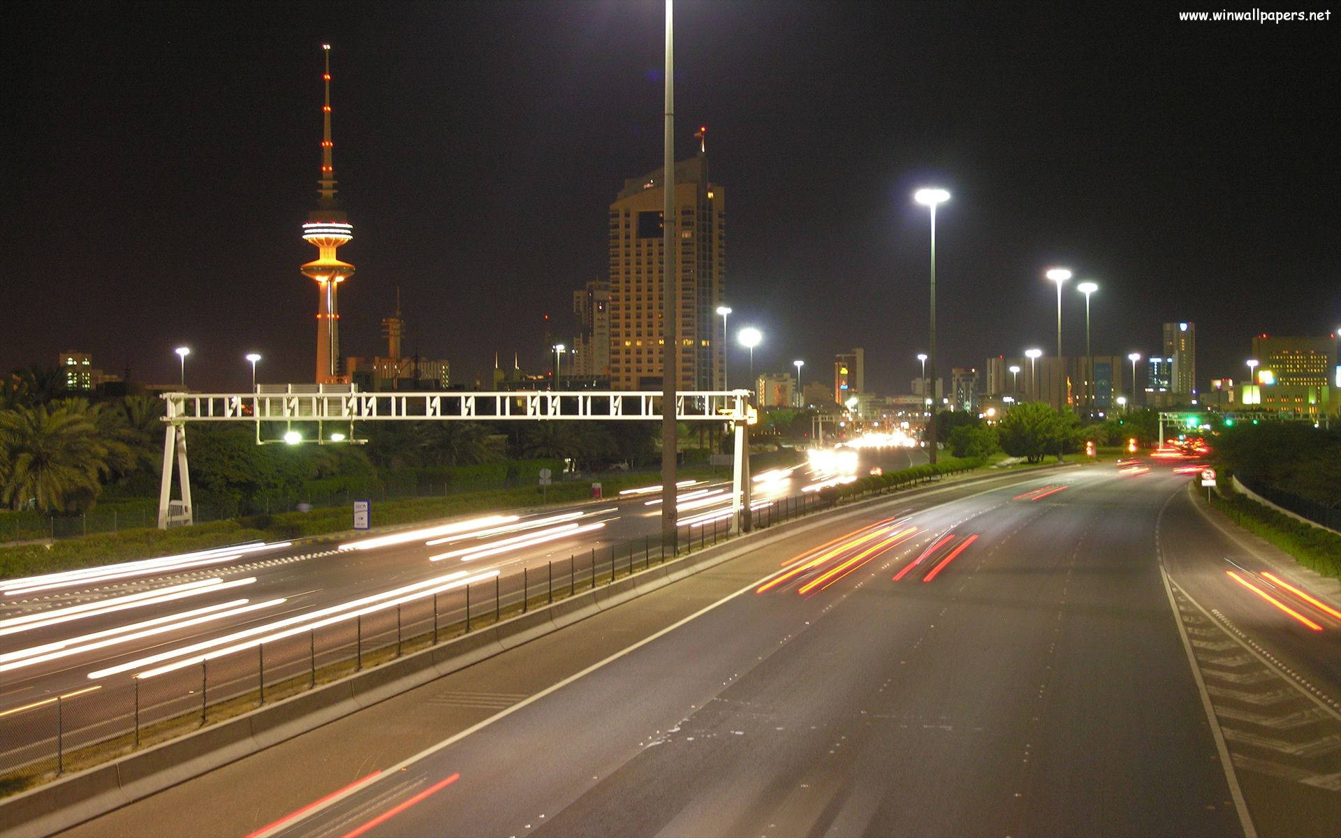 科威特繁忙街道 壁紙 — 夜間城市高速公路，有汽車的光跡和遠處的發光塔。