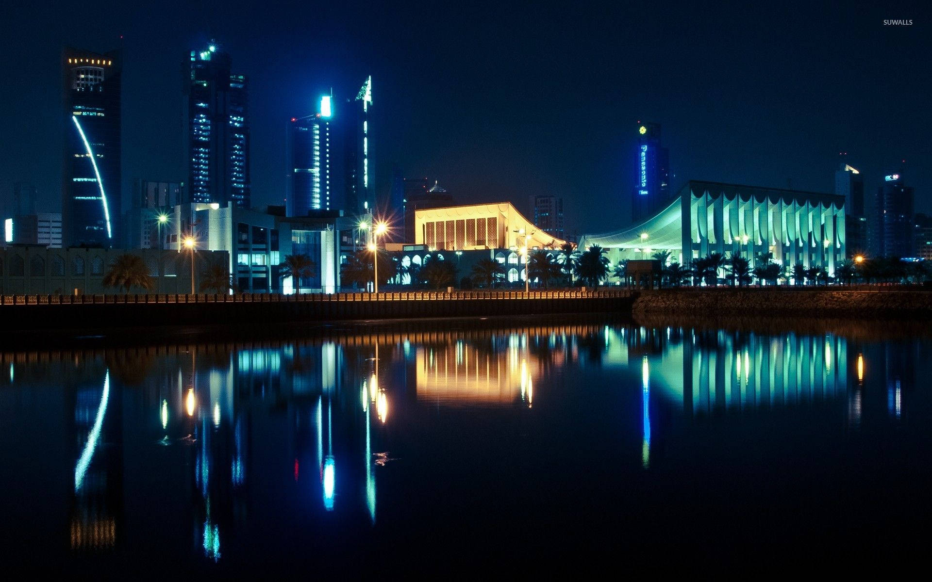 科威特議會大樓 壁紙 — 充滿活力的夜景城市景觀，燈火通明的摩天大樓和現代建築倒映在平靜的水面上。