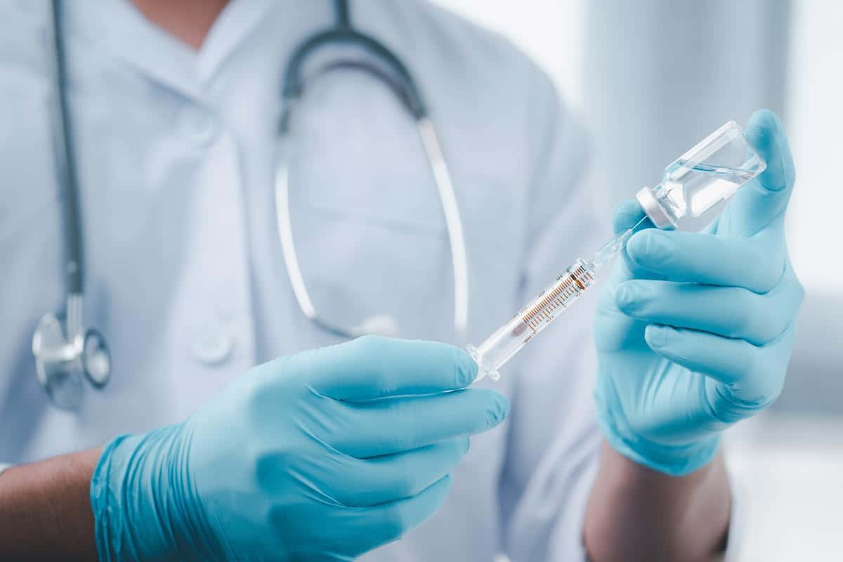 戴藍色手套的醫生正在用藥瓶和聽診器準備注射器。