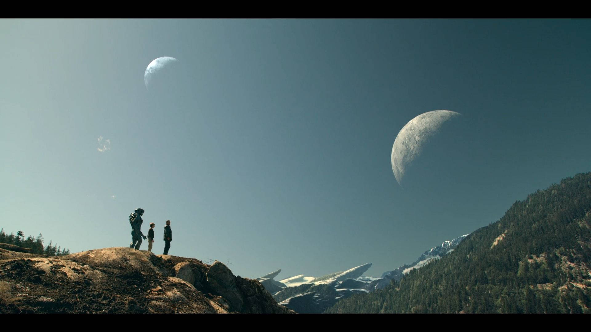 科幻系列《迷失太空》 壁紙 — 三個身影站在岩石山脊上，俯瞰著白雪覆蓋的山脈，天空中有兩個巨大的月亮。