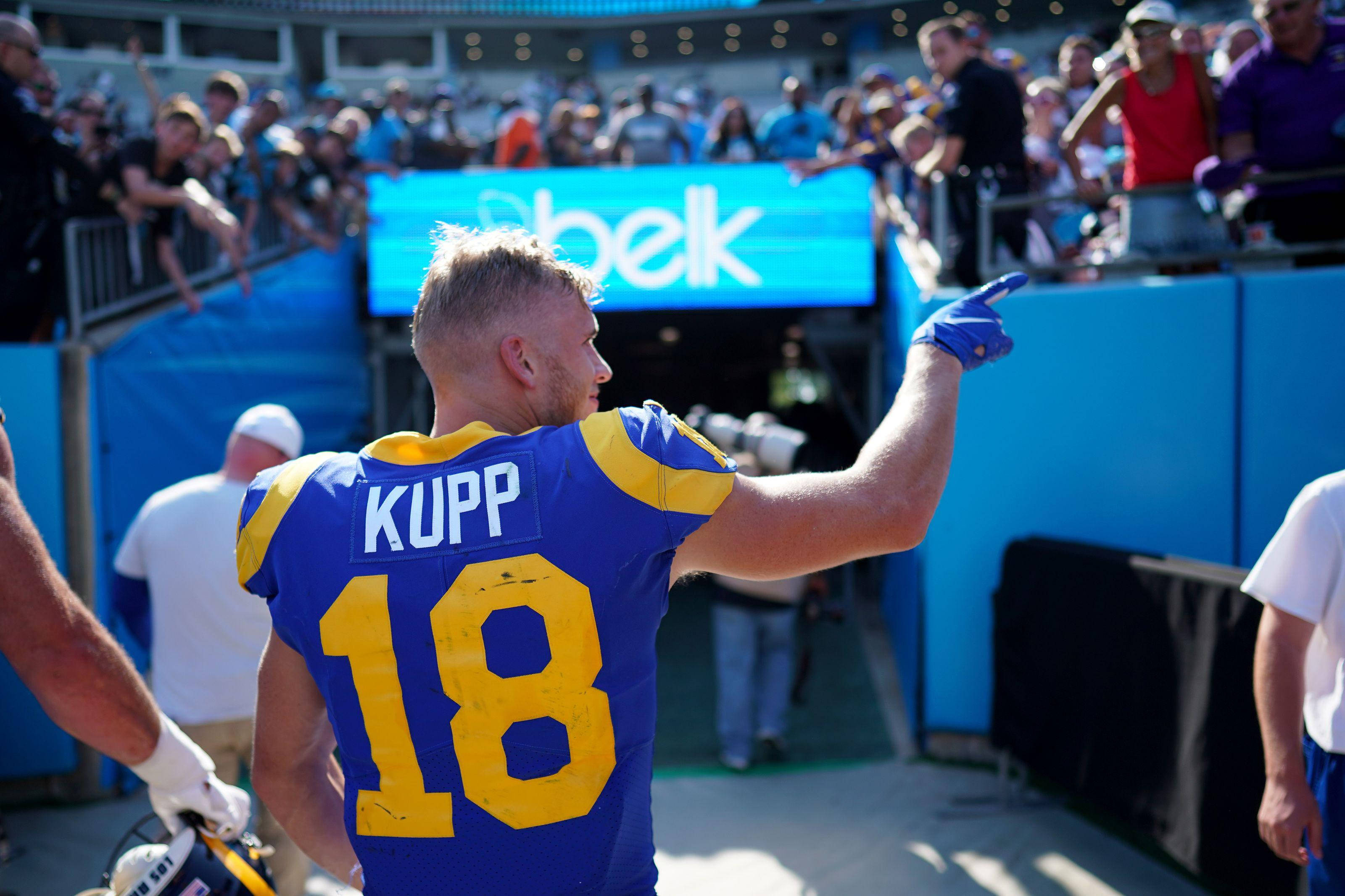 科珀·庫普 NFL 洛杉磯拉姆斯隊美式足球球迷攝影 壁紙 — 一名身穿藍黃球衣、背號18的足球運動員在陽光明媚的日子裡向體育場內的觀眾指點。