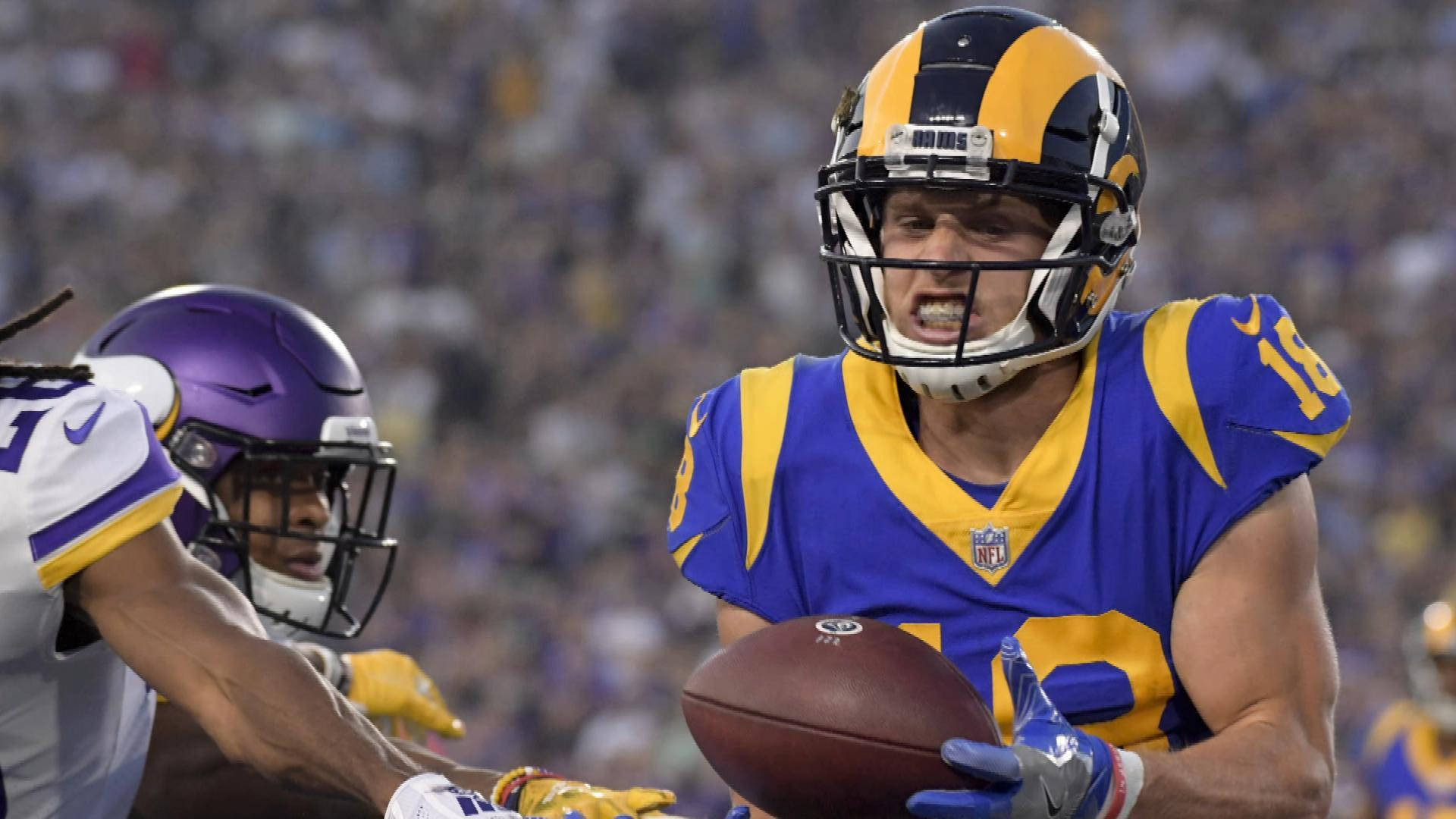 科珀·庫普 NFL 洛杉磯拉姆斯隊美式足球接球攝影 壁紙 — 一位身穿藍色和金色球衣的洛杉磯公羊隊美式足球員在明尼蘇達維京人隊紫色和白色防守球員的擒抱下緊緊抓住球。