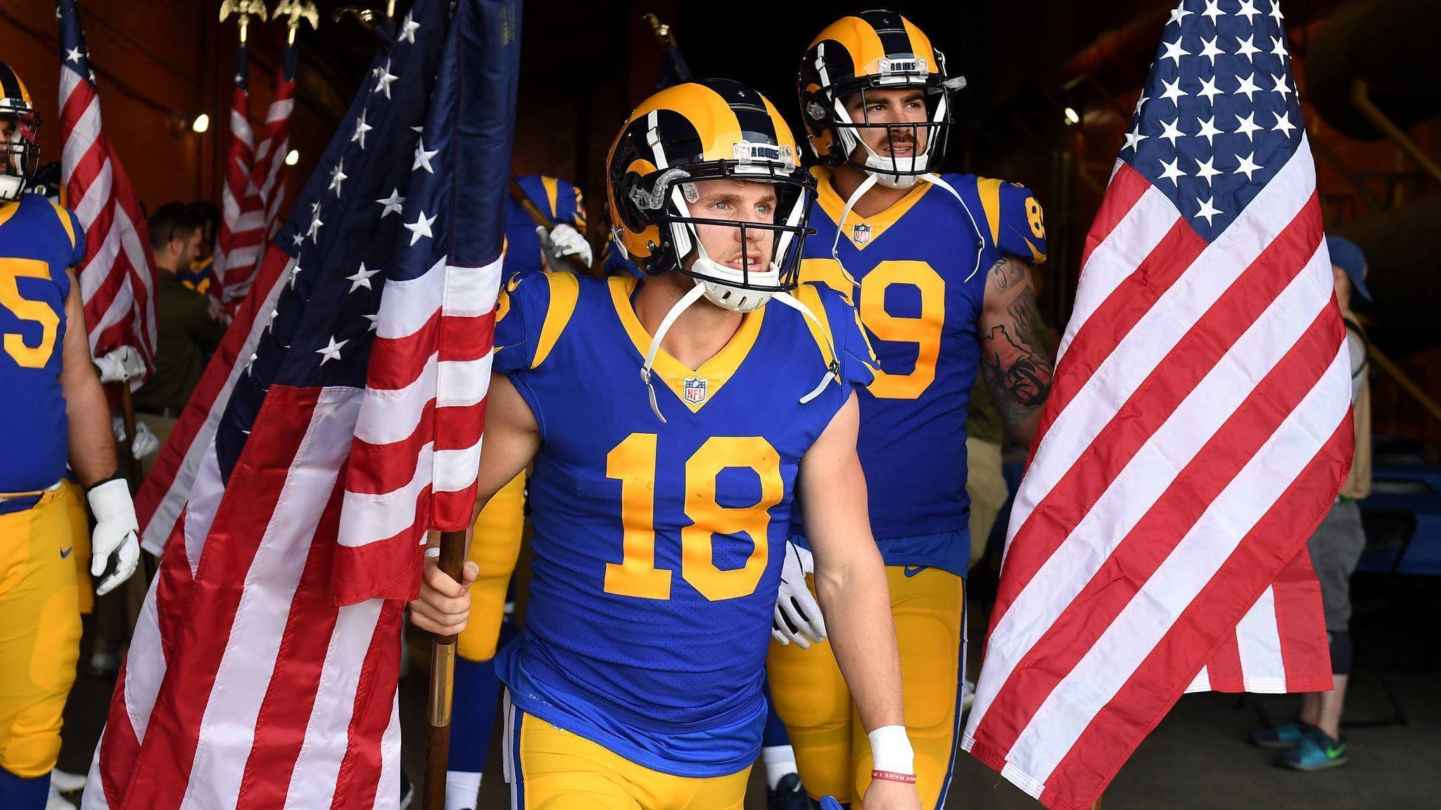 科珀·庫普 NFL 美國國旗拉姆斯隊美式足球 壁紙 — 穿著藍色和金色制服的美式足球NFL球員在比賽前莊嚴自豪地揮舞美國國旗。