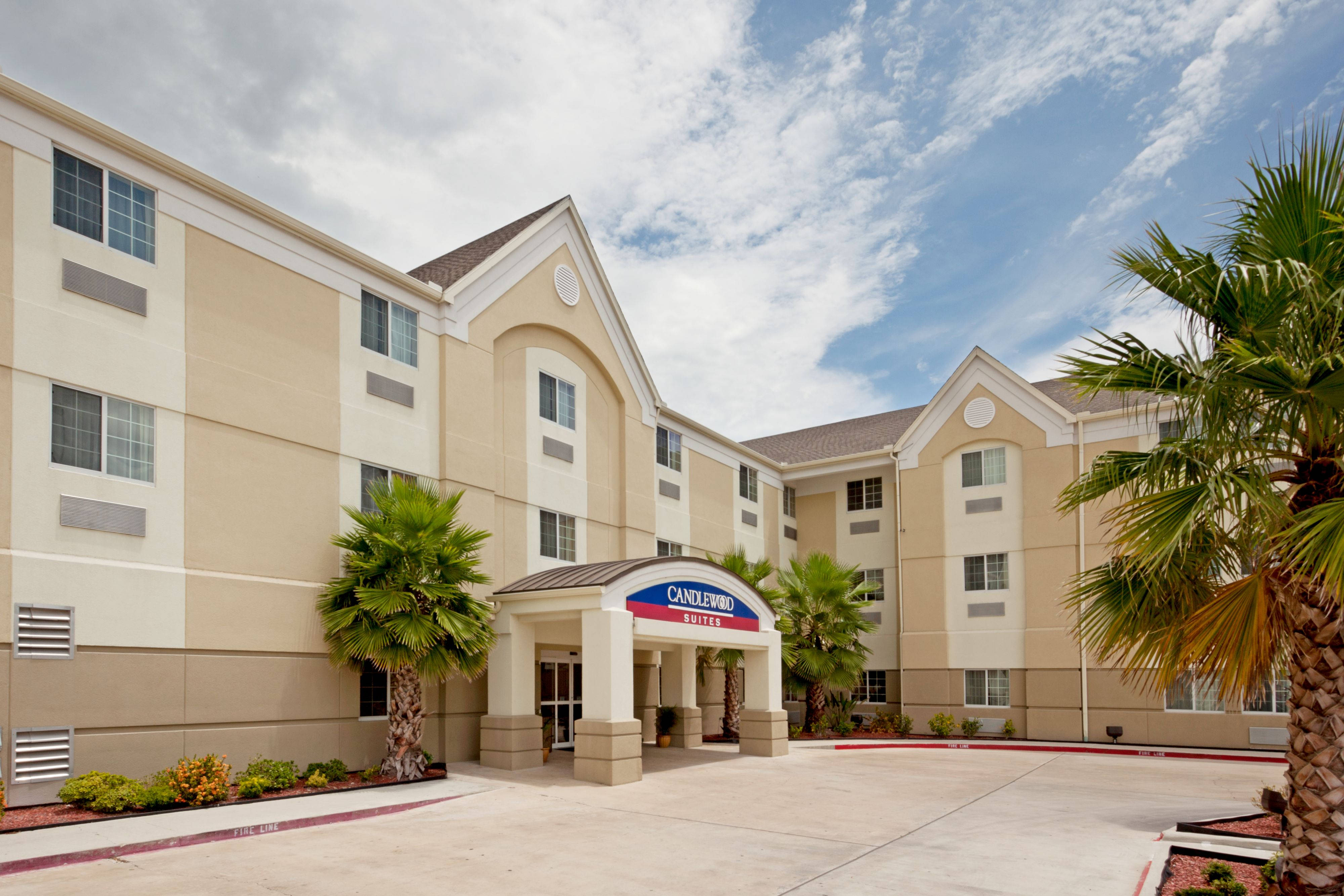 科珀斯克里斯蒂坎德伍德套房酒店 壁紙 — 米色Candlewood Suites酒店建築，天空局部多雲，入口兩旁種有棕櫚樹。