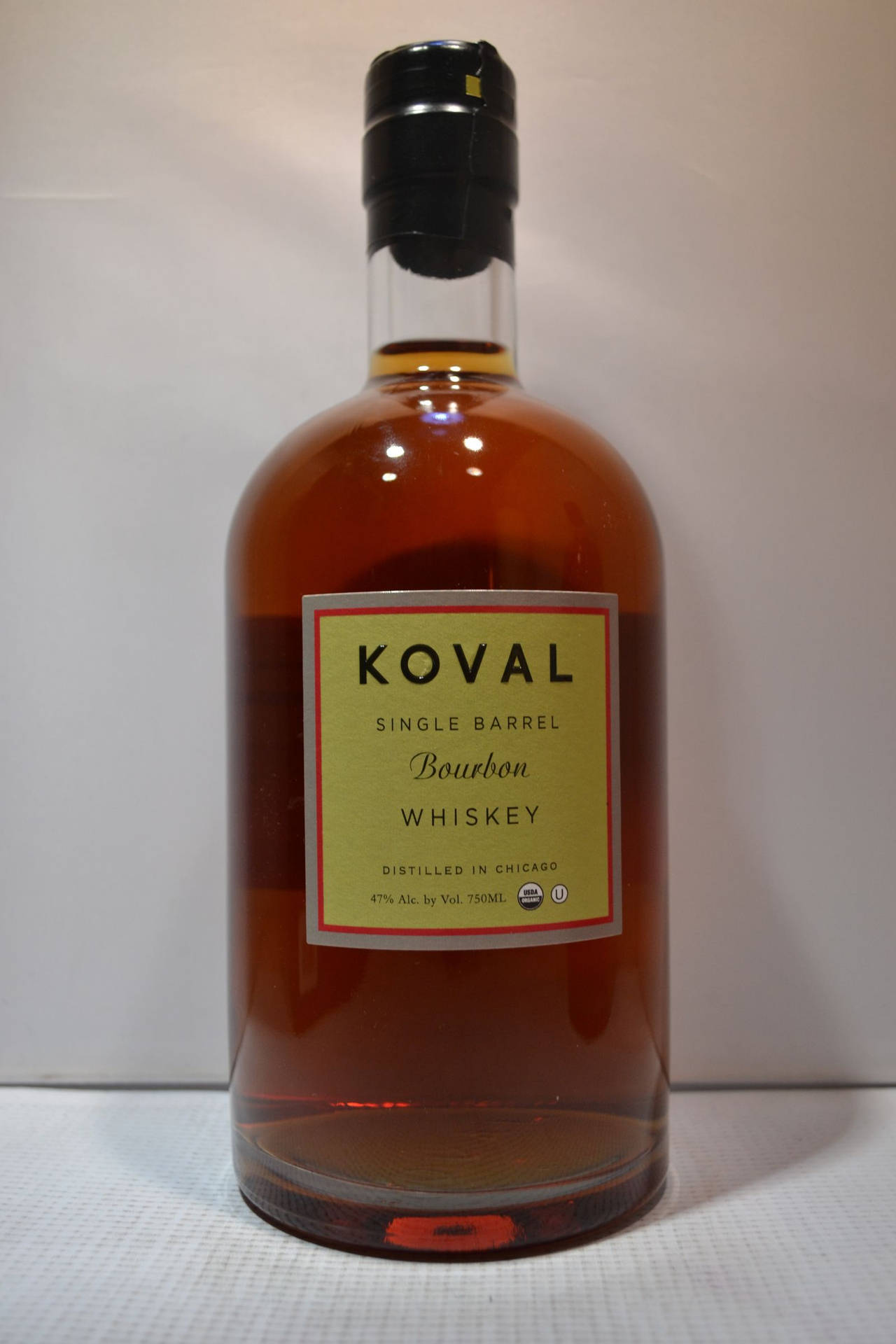 一瓶Koval波本威士忌，帶有琥珀色液體和黑色瓶蓋，放在白色表面上。