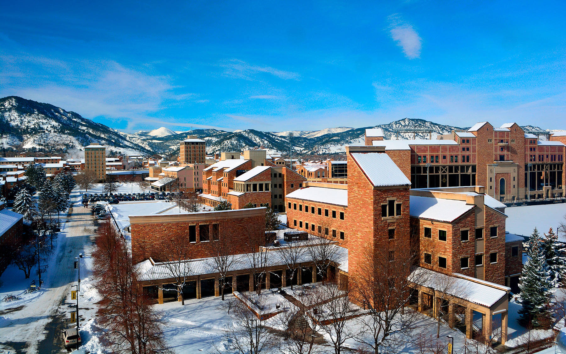 科羅拉多大學博爾德分校冬季雪景 壁紙 — 白雪覆蓋紅磚大學建築和光禿禿的樹木，在清澈的藍天下，遠處有積雪的山峰。