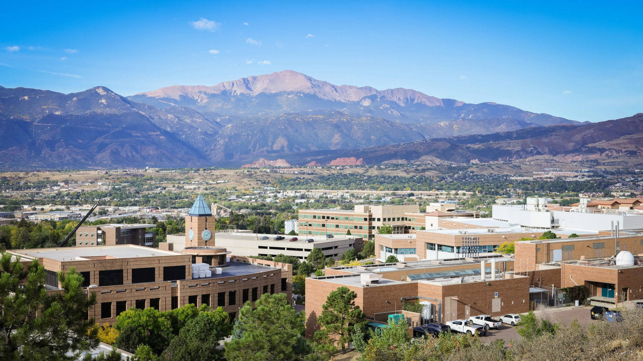 科羅拉多大學與山景壯麗風光 壁紙 — 大學校園坐落於山谷中的全景景觀，雄偉的山脈在清澈的藍天下聳立。