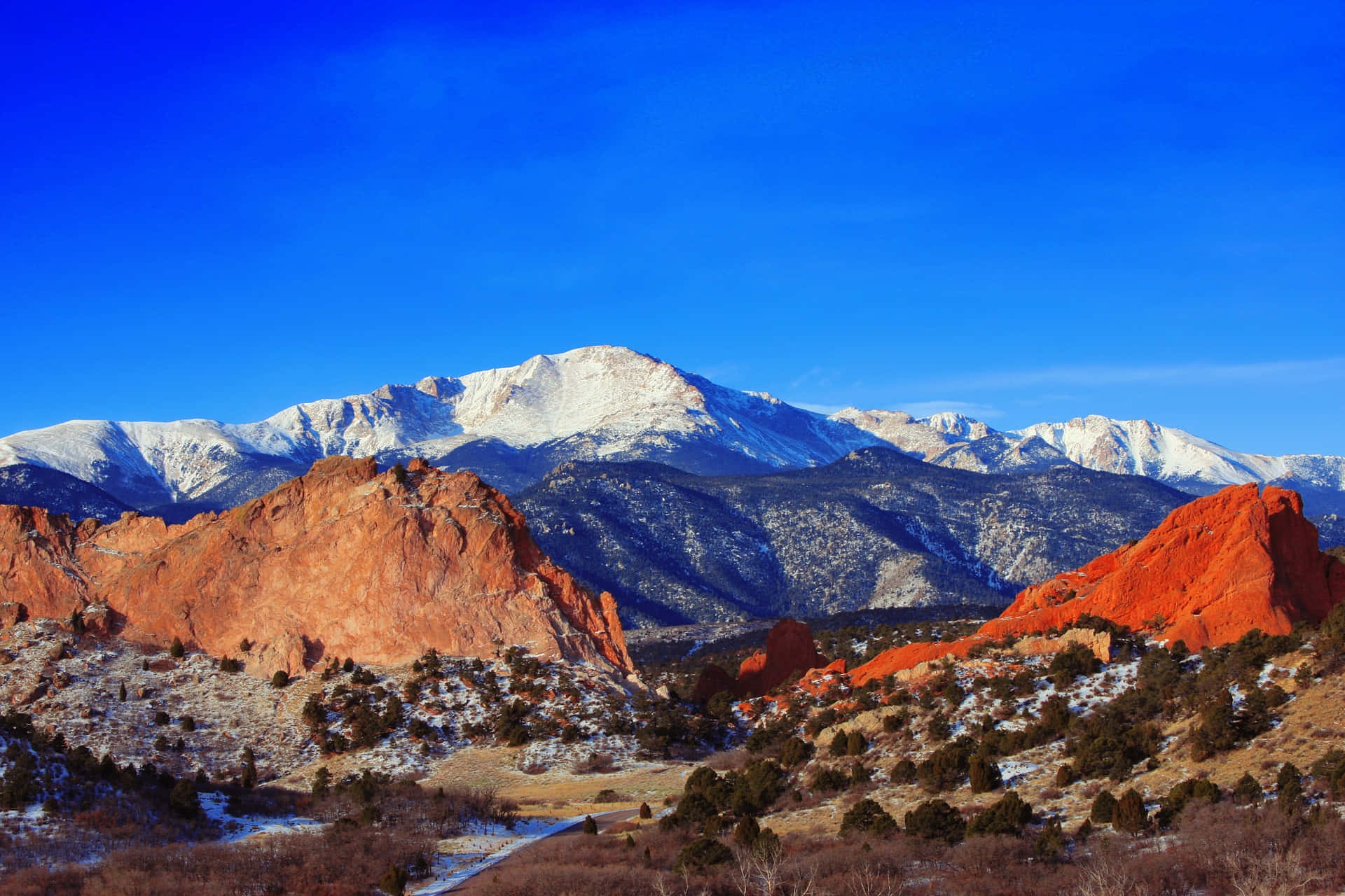 科羅拉多山的壯麗景色 壁紙 — 白雪覆蓋的山峰在清澈的藍天下，從鮮紅色的岩層後方升起。