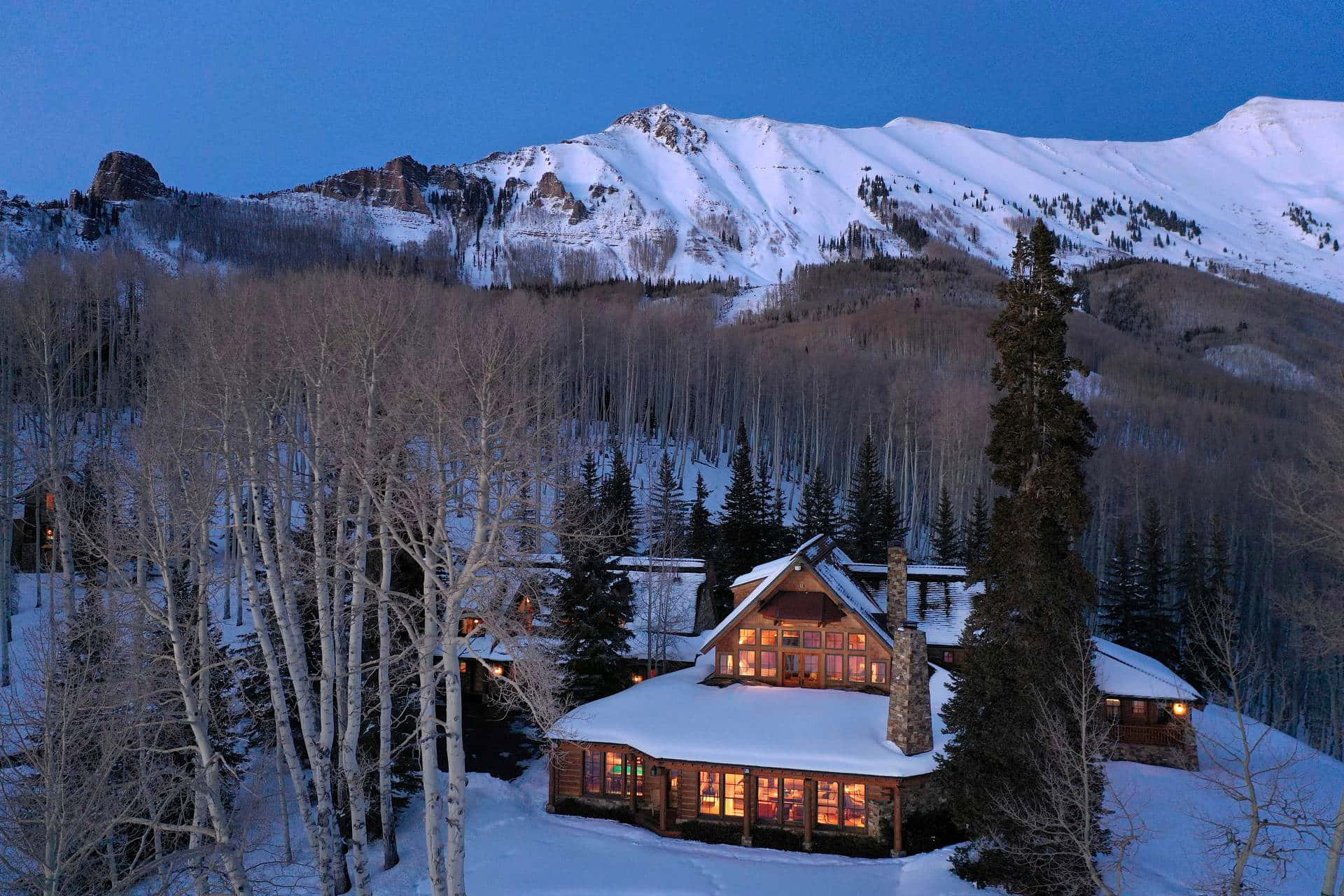 科羅拉多山脈的壯觀山景 壁紙 — 一間舒適的雪覆蓋小屋在暮色山景和光禿的白楊樹襯托下溫暖地發光。