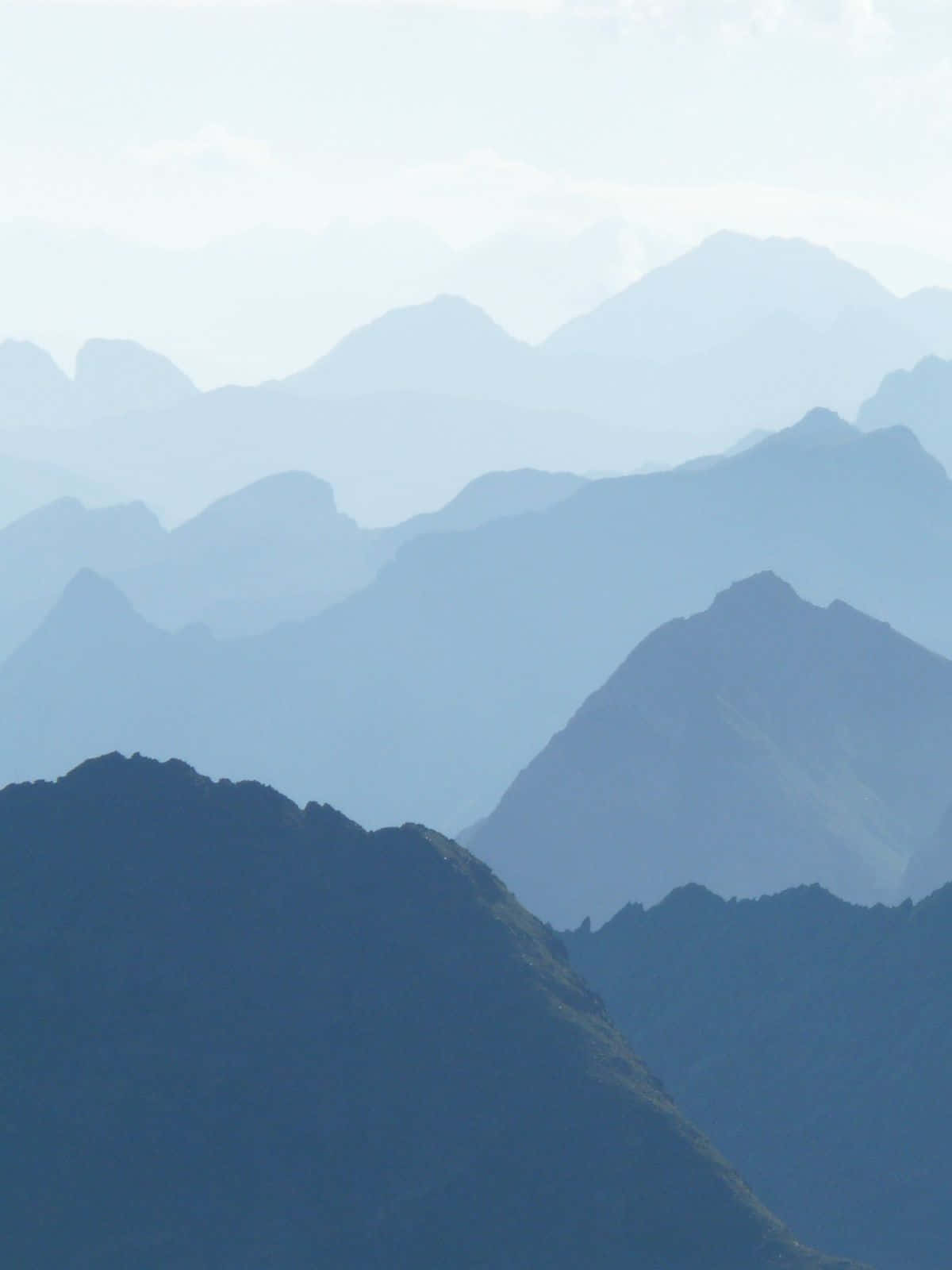科羅拉多州壯麗山景與劇烈天空 壁紙 — 層層疊疊的山峰在柔和日光下逐漸融入迷濛的藍色薄霧中。