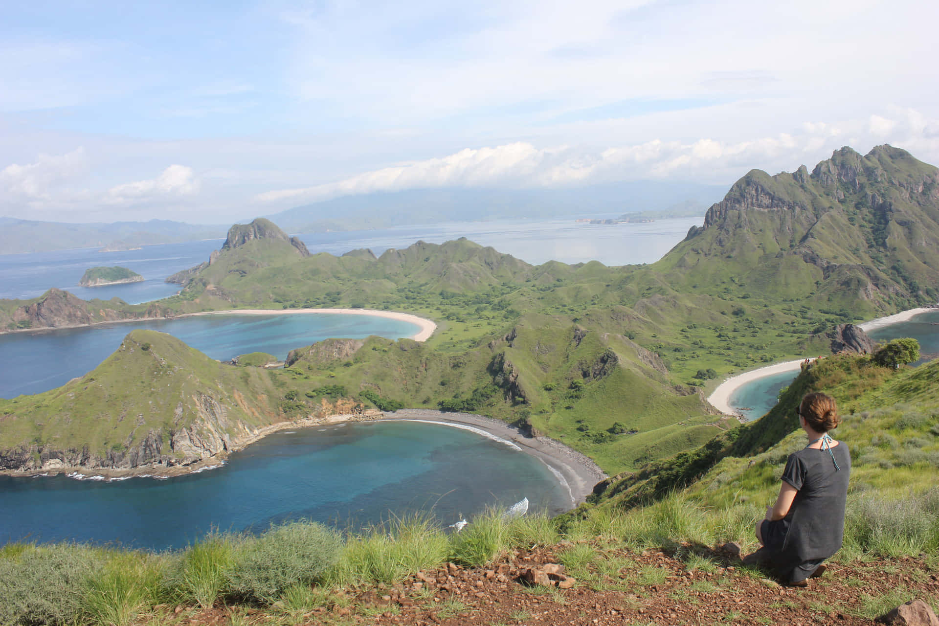 人坐在懸崖邊緣俯瞰海岸海灣和綠色山脈