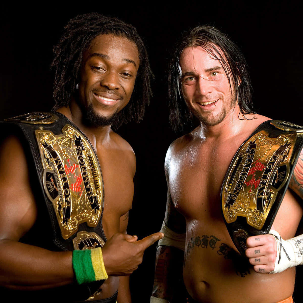 科菲·金斯顿與CM Punk 2008 壁紙 — 兩位微笑的WWE雙打冠軍自信地在黑色背景前擺姿勢，展示他們的金色和黑色冠軍腰帶。