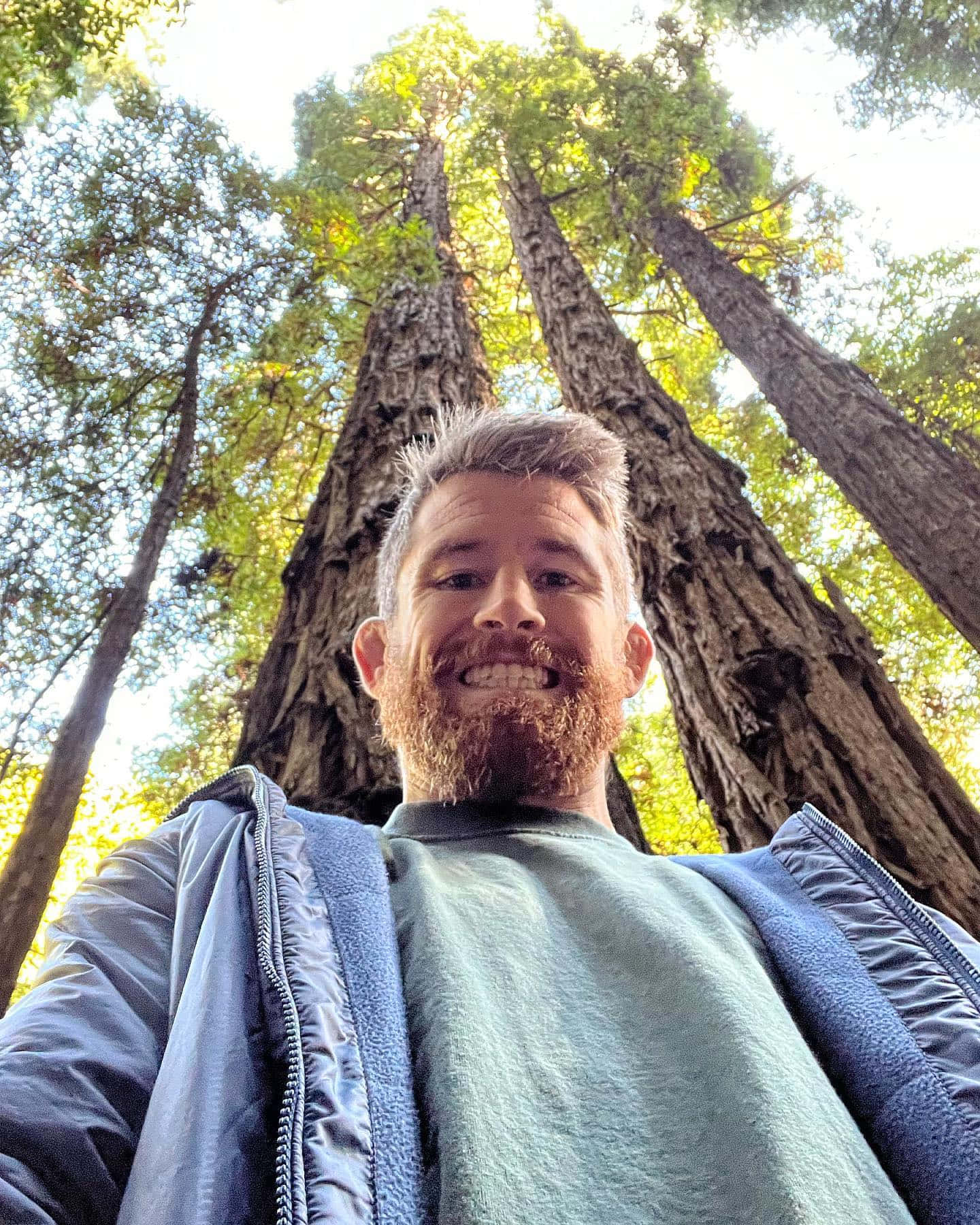 喺森林中巨型紅杉樹之間微笑嘅留鬍鬚男人。