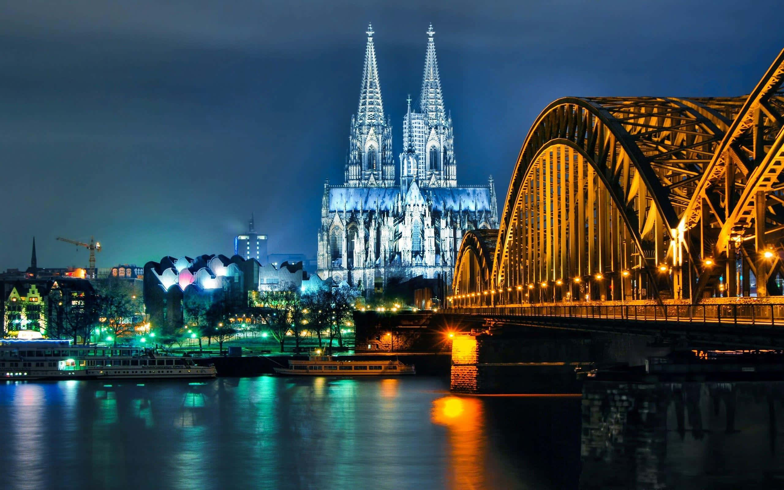 Germany 桌布 壁紙 — 科隆大教堂和霍亨索倫橋在萊茵河上夜間亮燈的壯麗景色，帶有倒影。