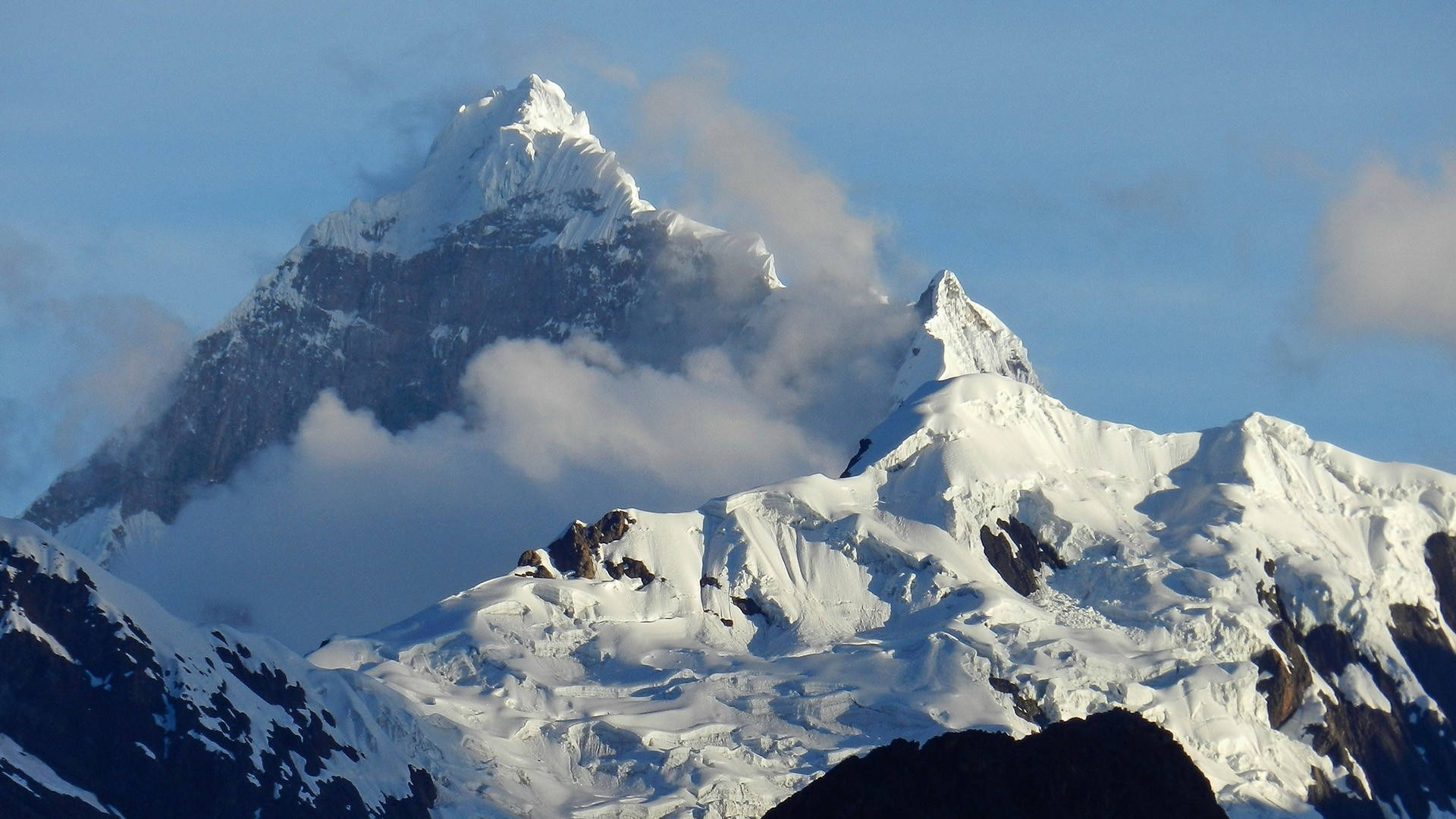 雪山峰頂聳立於雲層之上，藍天背景