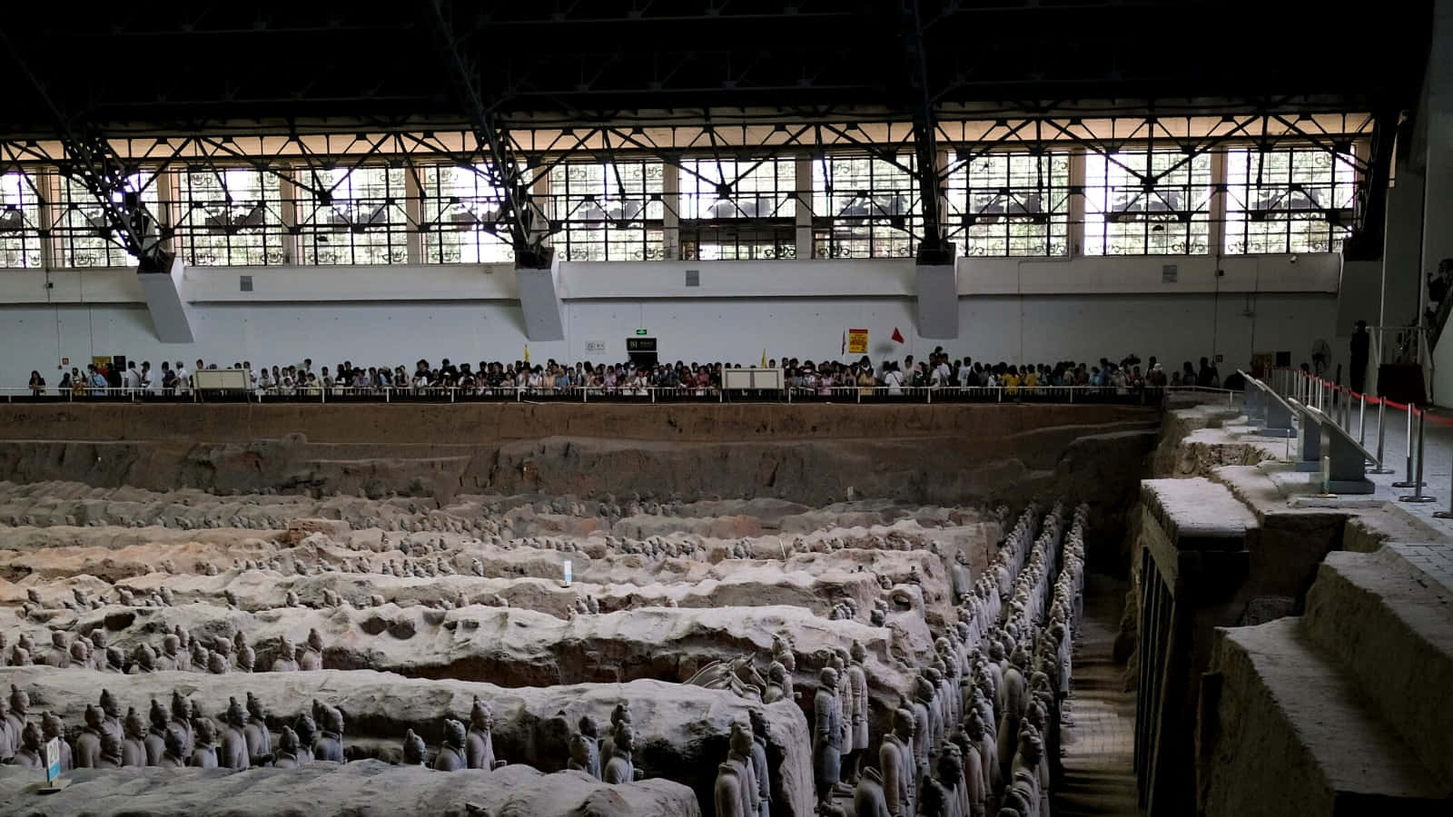 秦俑紀念藝術博物館內部 壁紙 — 一排排古代兵馬俑矗立在寬闊的博物館發掘坑中，遊客從高架步道上觀看。