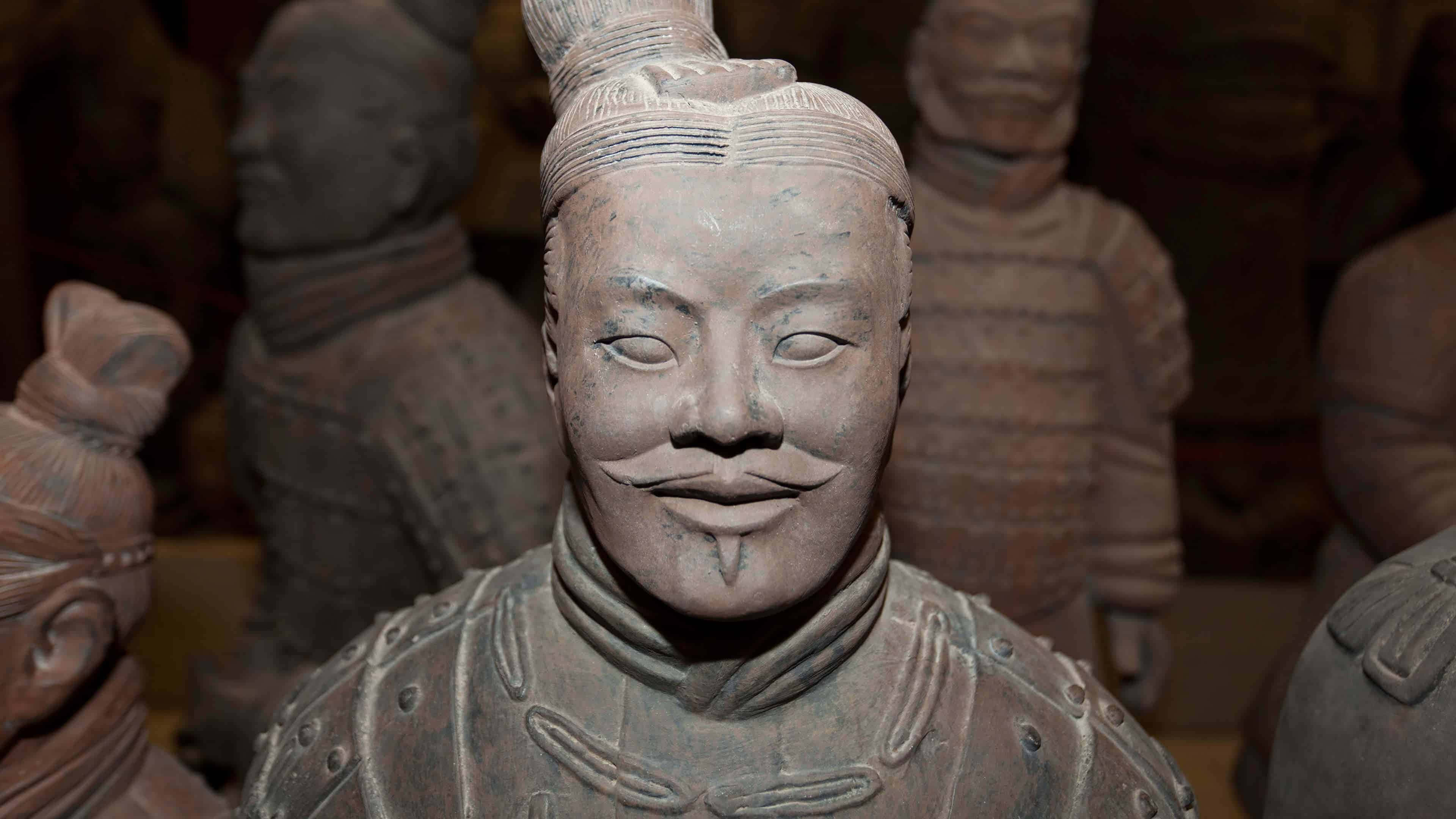 秦俑雕塑細節特寫 壁紙 — 博物館環境中，一個表情平靜、盔甲精細的兵馬俑雕像特寫。