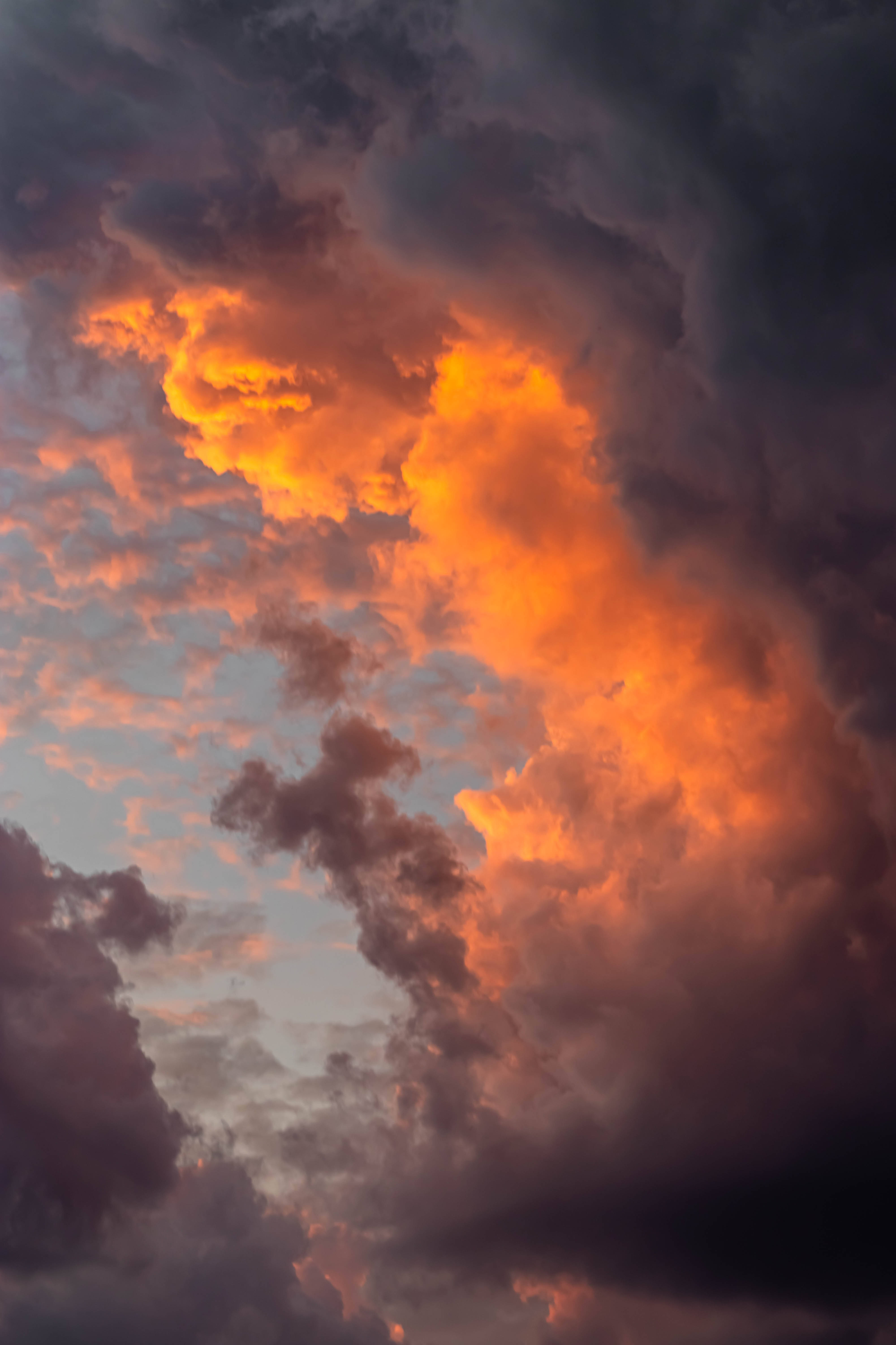 積雨雲與唯美天空 壁紙 — 戲劇性的雲朵在暮色天空中發出火橙色光芒，帶有深紫色和灰色的陰影。