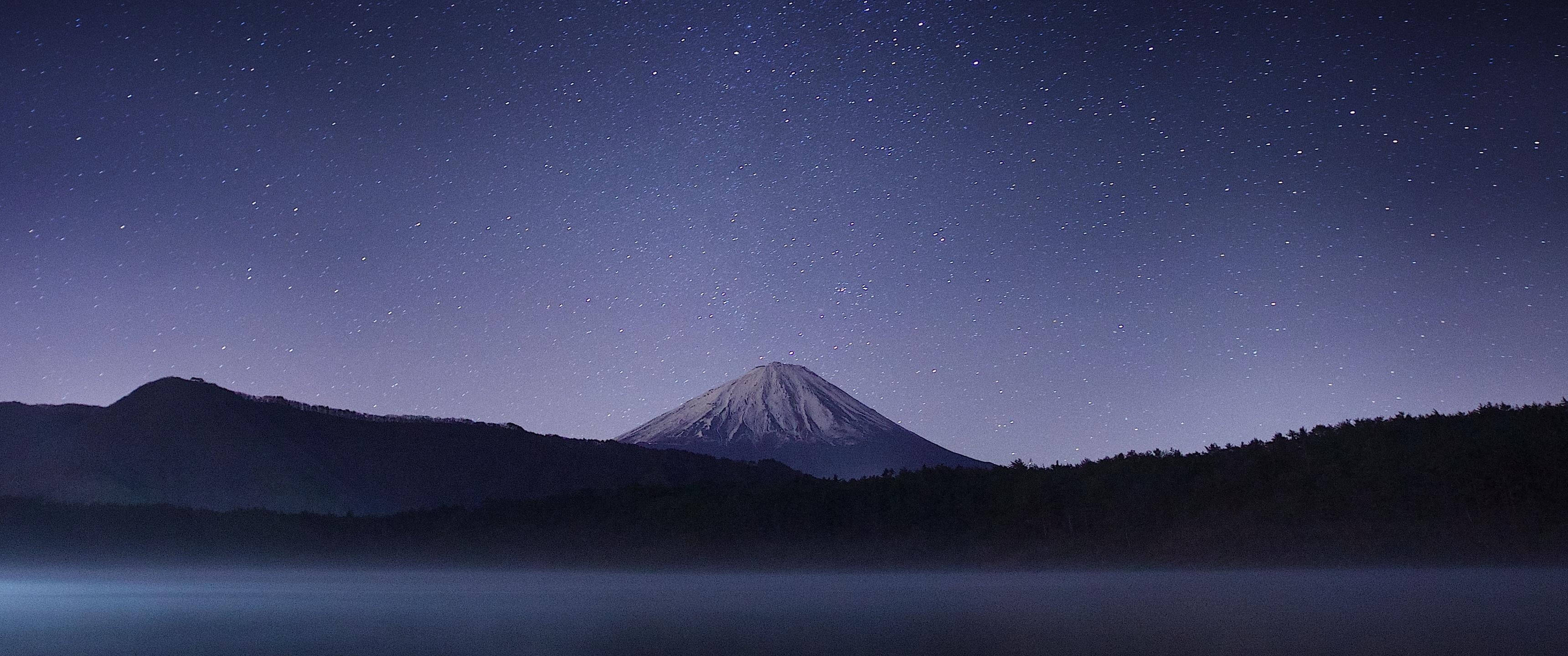 自然 桌布 壁紙 — 積雪的富士山在繁星點點的夜空下，在霧氣瀰漫的湖面上寧靜地聳立。