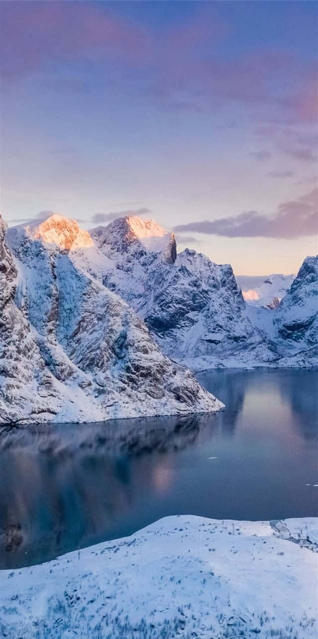 Norway 桌布 壁紙 — 積雪的山峰在柔和的紫色天空下，金色的日出光芒映照在平靜的冰湖上，閃閃發光。