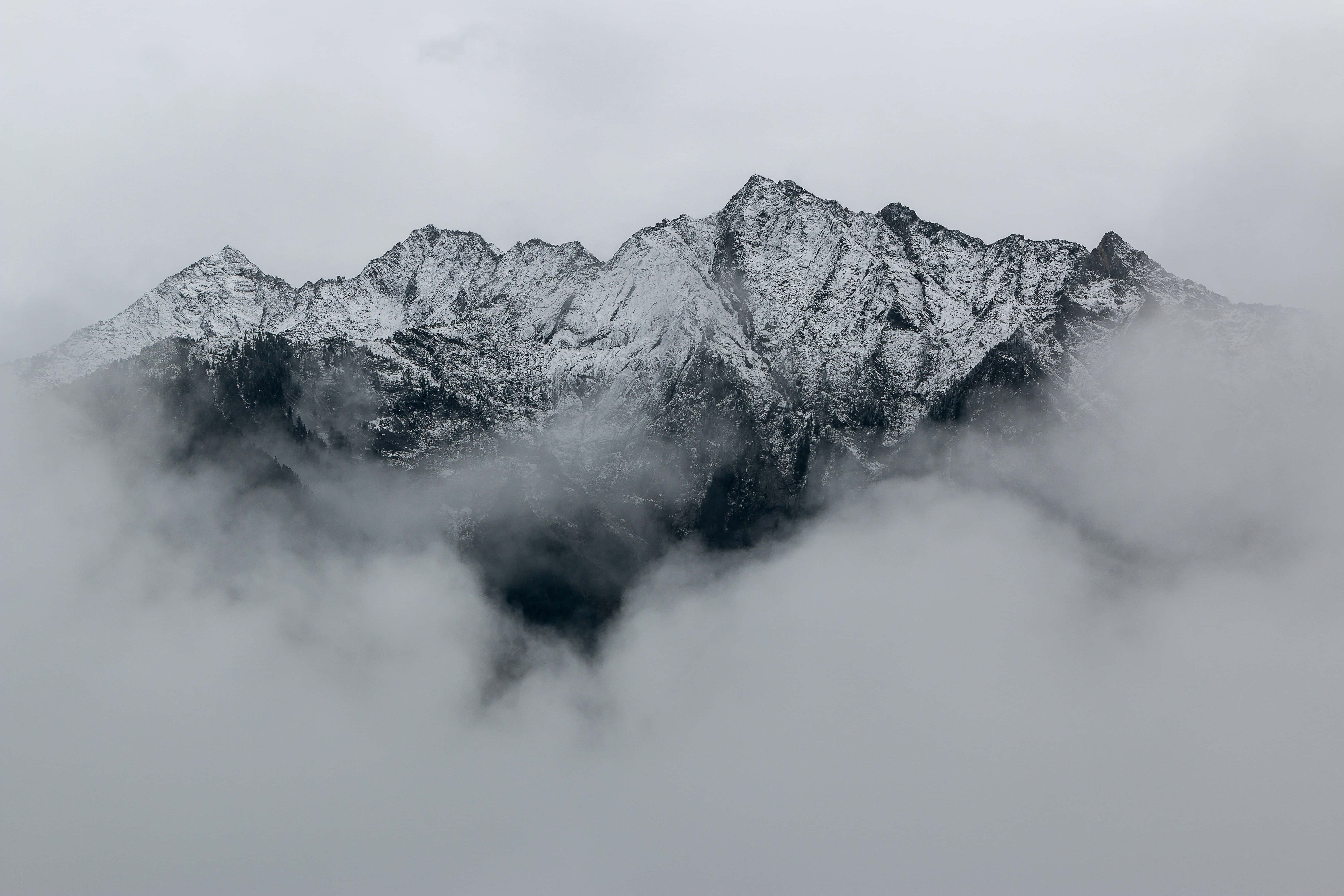 macOS 桌布 壁紙 — 積雪的山峰穿過濃霧，在陰天之下營造出寧靜而神秘的高山景象。