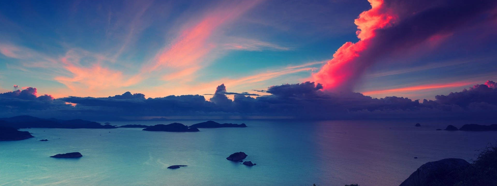 平靜海面上的鮮豔日落，散落島嶼和多彩雲彩。