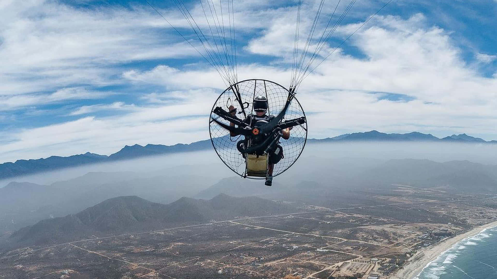 人在有雲的山脈和海洋上空飛滑翔傘